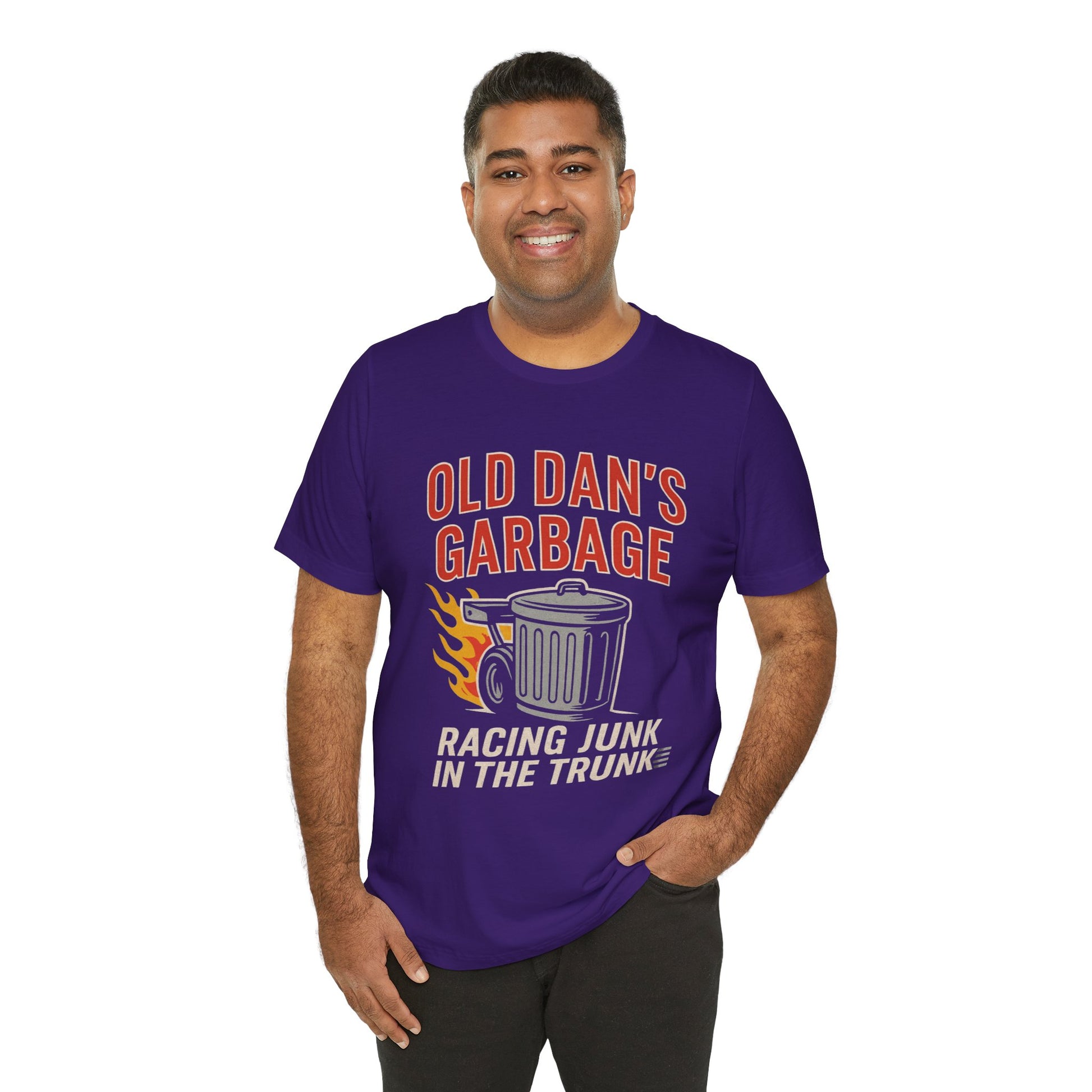 Person wearing a purple graphic T‑shirt featuring the bold red and white text “Old Dan’s Garbage” above a flaming garbage can illustration, with the tagline “Racing Junk in the Trunk” below. Funny drag racing parody shirt with retro racing flames, checkered flag background, and humor‑driven hot rod style, perfect for car enthusiasts and gearhead apparel fans.