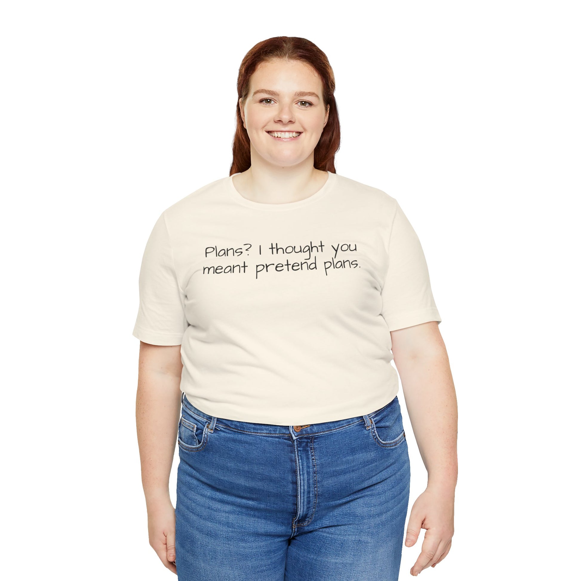 Person wearing a beige t-shirt with text 'Plans? I thought you meant pretend plans' and blue jeans on a white background