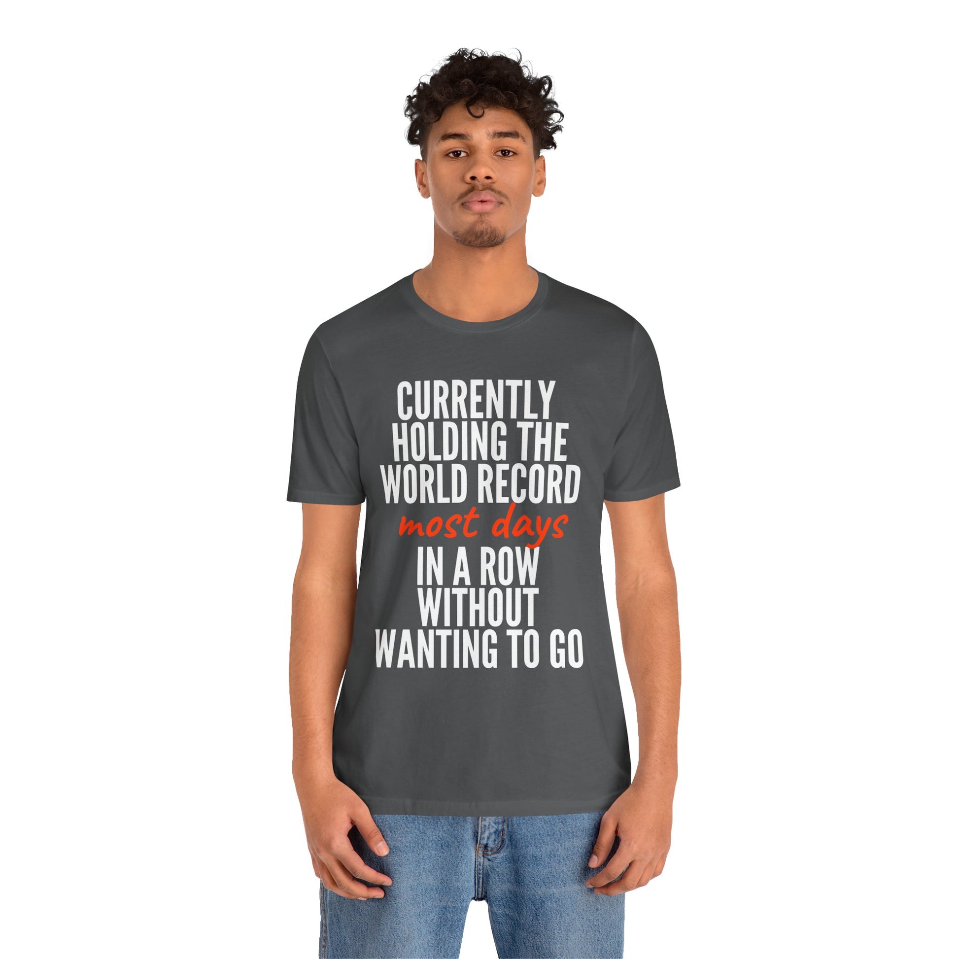 Person wearing a dark gray t-shirt with humorous text 'Currently holding the world record most days in a row without wanting to go' design on a white background