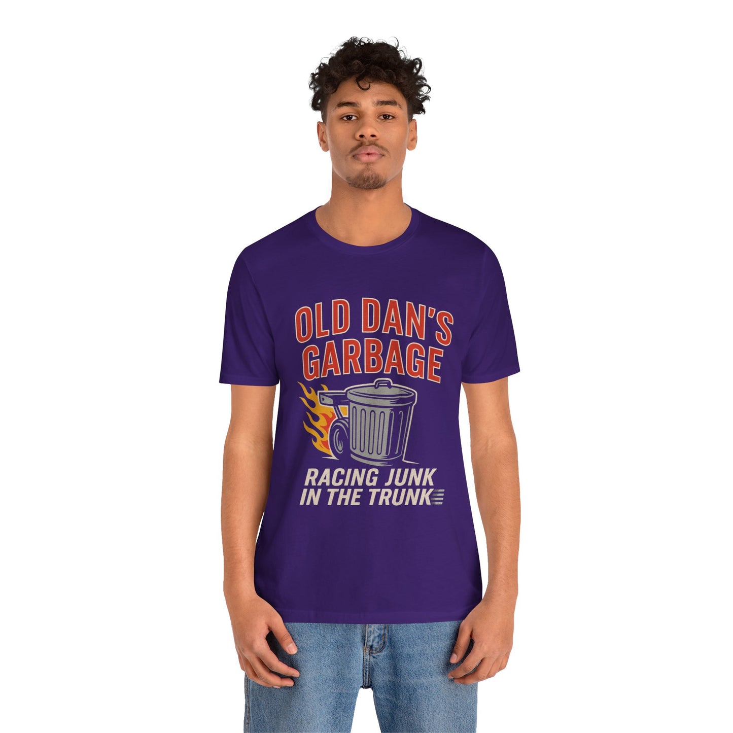 Person wearing a purple graphic T‑shirt featuring the bold red and white text “Old Dan’s Garbage” above a flaming garbage can illustration, with the tagline “Racing Junk in the Trunk” below. Funny drag racing parody shirt with retro racing flames, checkered flag background, and humor‑driven hot rod style, perfect for car enthusiasts and gearhead apparel fans.