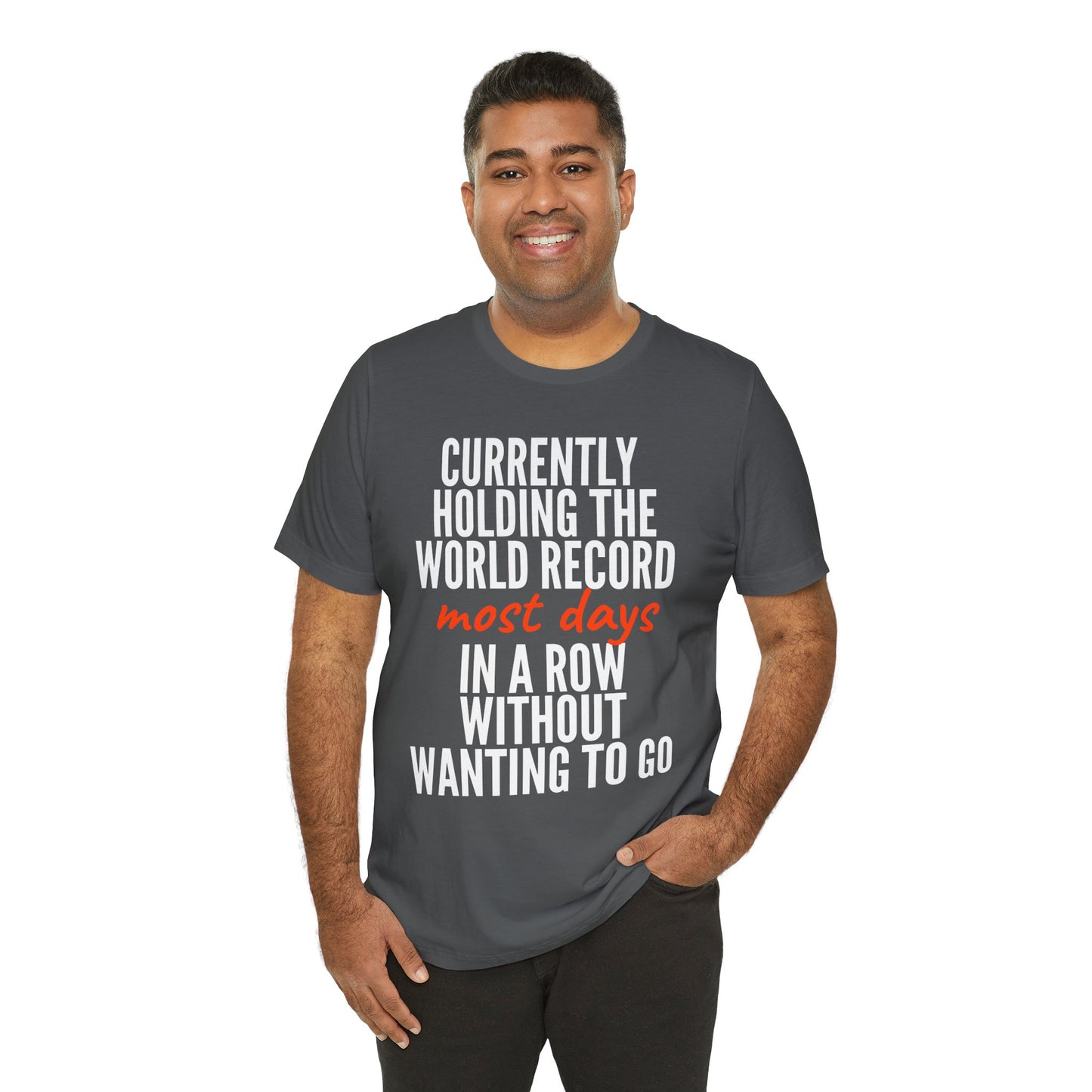 Man wearing a gray t-shirt with humorous text 'Currently holding the world record most days in a row without wanting to go' design on a white background