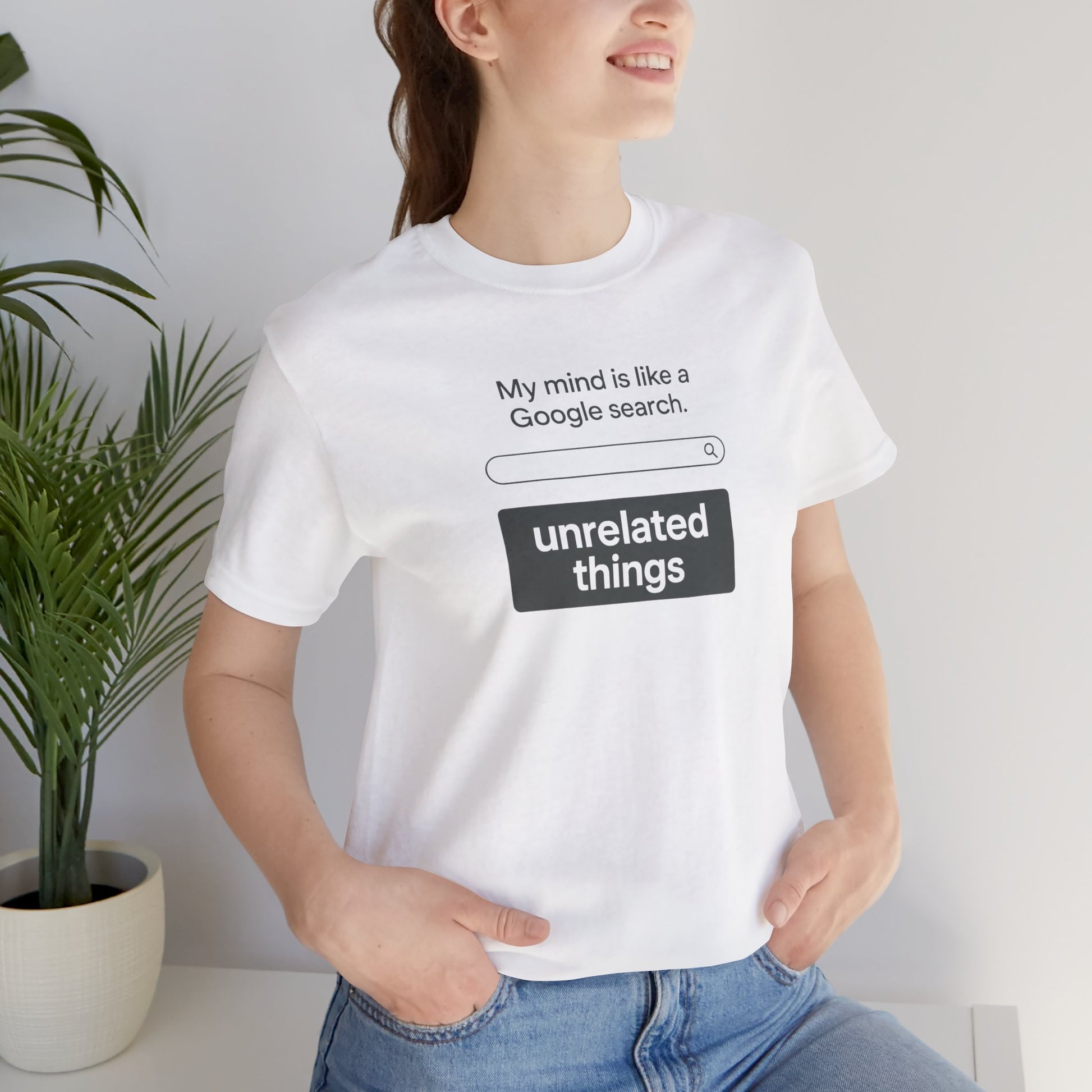 Person wearing a white t-shirt with humorous text design, standing indoors next to a plant. Shirt graphic is a search bar with text above that says, 'My mind is like a Google search' and text below says, 'unrelated things.'
