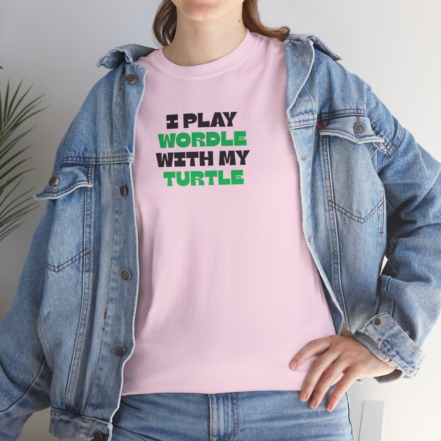 Person wearing a pink t-shirt with text and a denim jacket indoors.