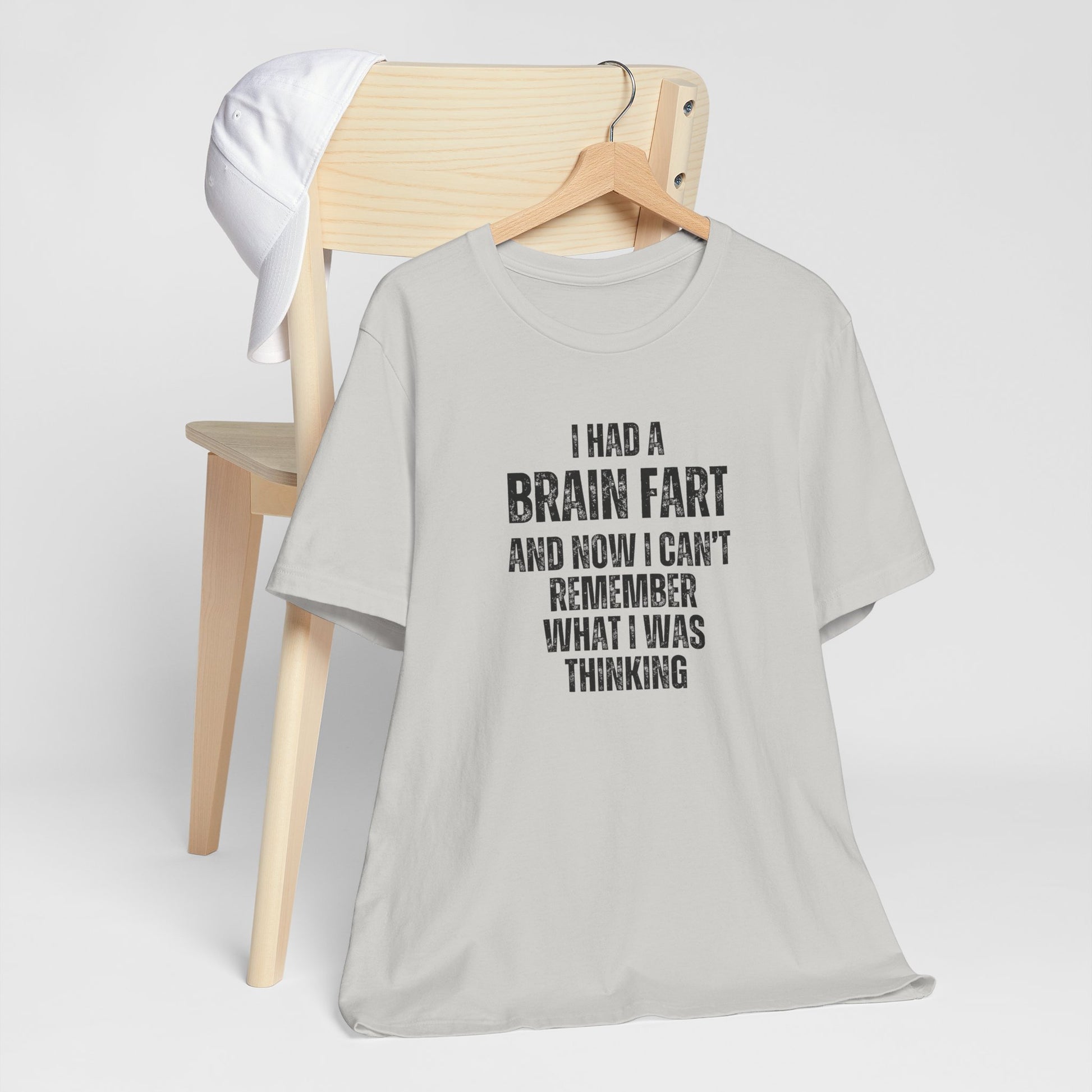 Gray t-shirt with humorous text 'I had a brain fart and now I can't remember what I was thinking' on a wooden chair against a white background