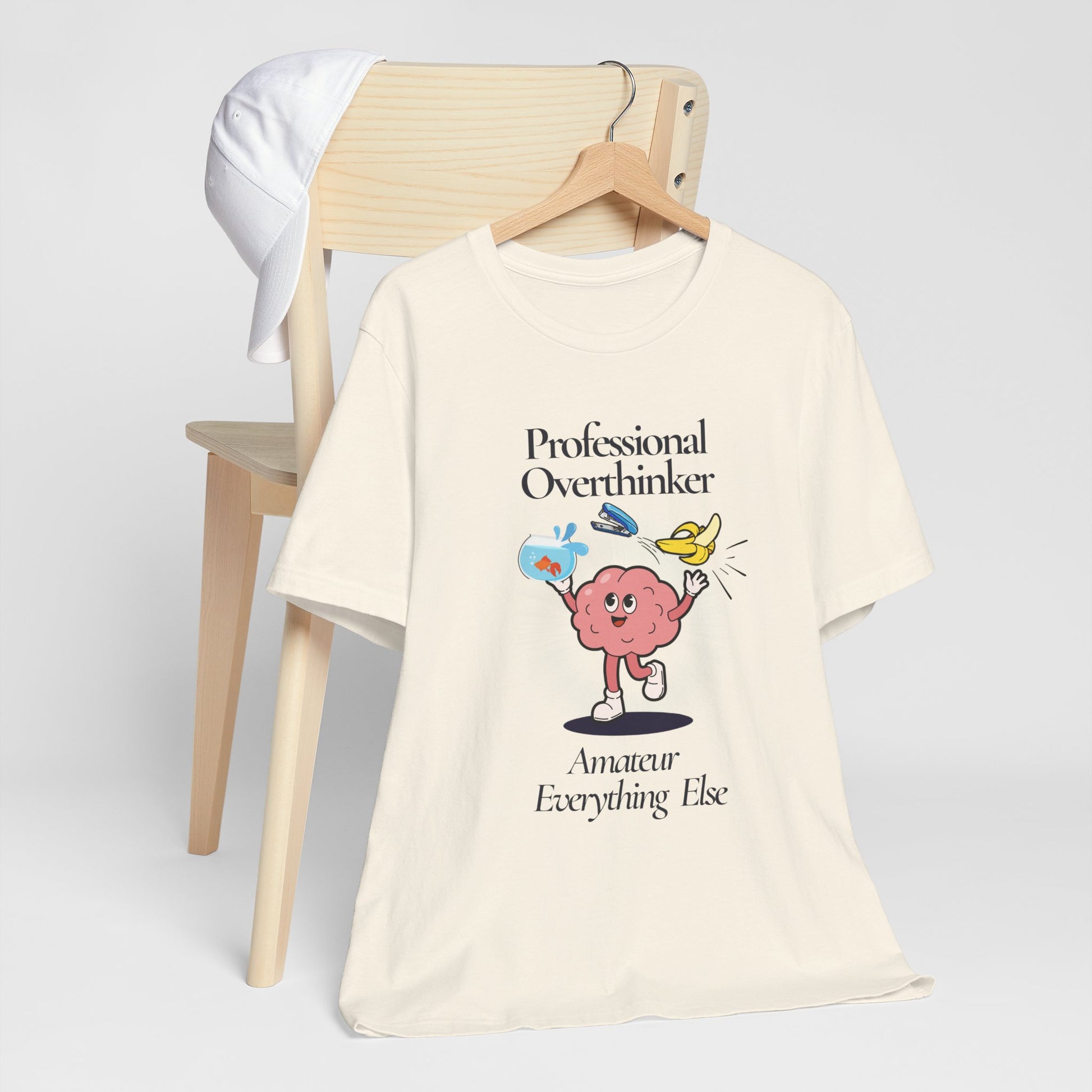 Beige t-shirt with a graphic design and text 'Professional Overthinker, Amateur Everything Else' on a white background
