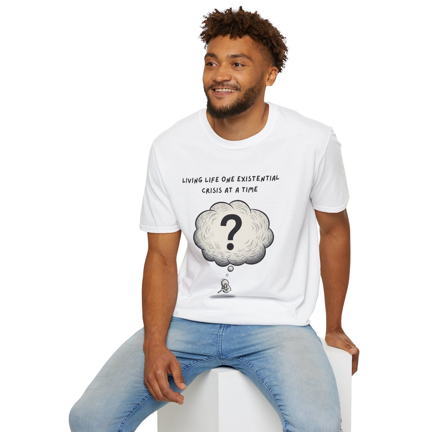 Man wearing a white t-shirt with a graphic and text  'Living Life One Existential Crisis At A Time', sitting on a white stool against a white background.