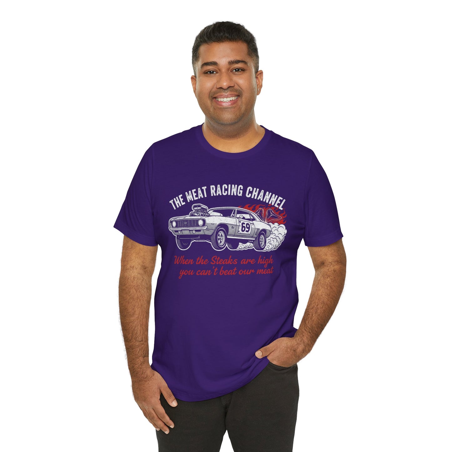 Person wearing a purple Bella+Canvas 3001 T‑shirt featuring a bold drag racing graphic. The design shows a vintage muscle car with the number 69, white smoke and red flames, the distressed white title “The Meat Racing Channel” above, and the red script tagline “When the Steaks are high you can’t beat our meat” below. Funny drag racing parody shirt with retro hot rod style, perfect for car enthusiasts, gearheads, and humor‑driven racing apparel fans.