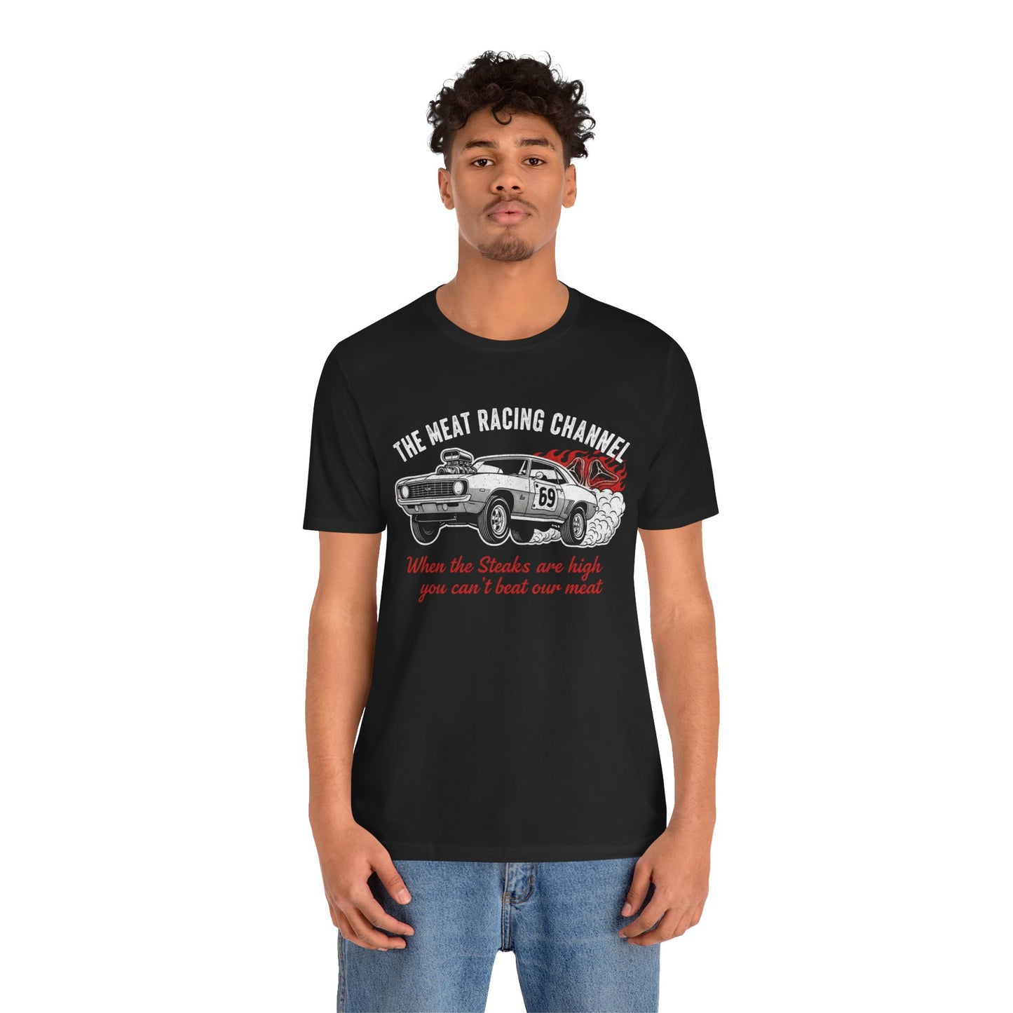 Person wearing a black Bella+Canvas 3001 T‑shirt featuring a bold drag racing graphic. The design shows a vintage muscle car with the number 69, white smoke and red flames, the distressed white title “The Meat Racing Channel” above, and the red script tagline “When the Steaks are high you can’t beat our meat” below. Funny drag racing parody shirt with retro hot rod style, perfect for car enthusiasts, gearheads, and humor‑driven racing apparel fans.