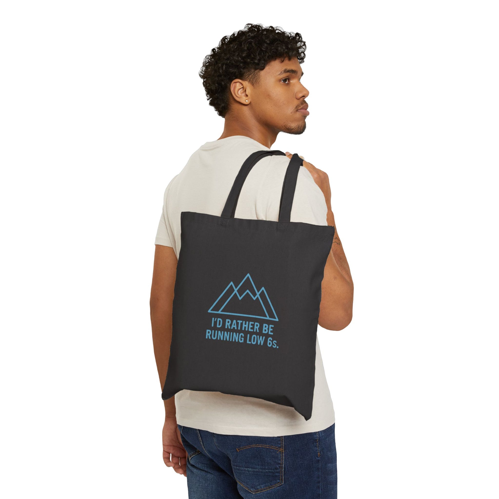 Man carrying a black tote bag with text 'I'd rather be running low 6s' and mountain graphic on a white background