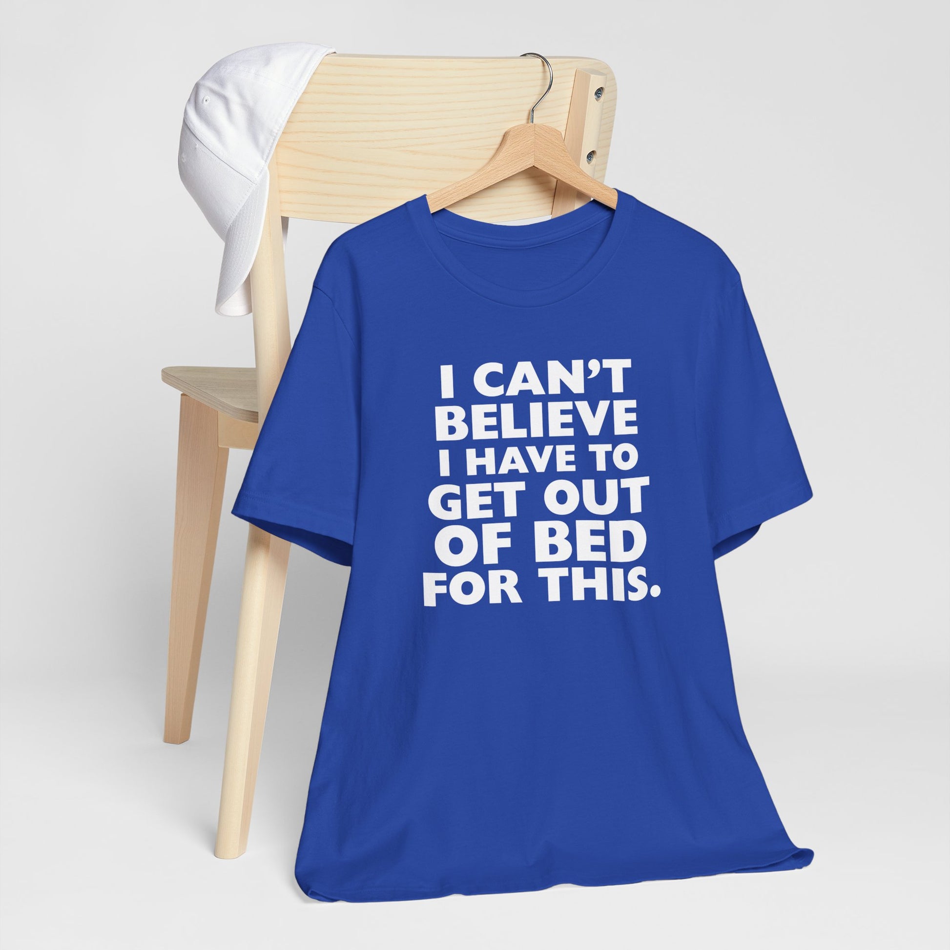 Blue t-shirt with white text 'I can't believe I have to get out of bed for this' on a white background