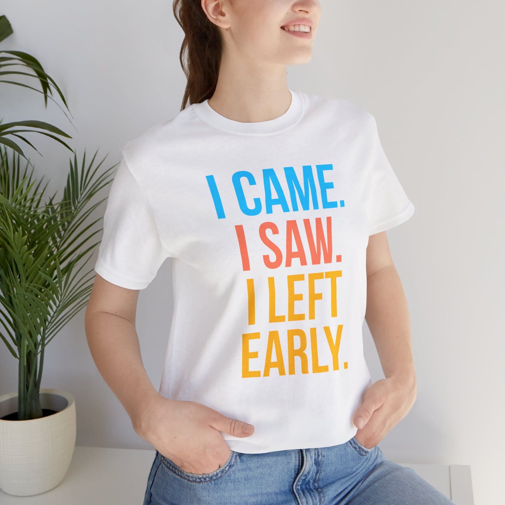 Person wearing a white t-shirt with colorful text 'I CAME. I SAW. I LEFT EARLY.' in a casual setting.