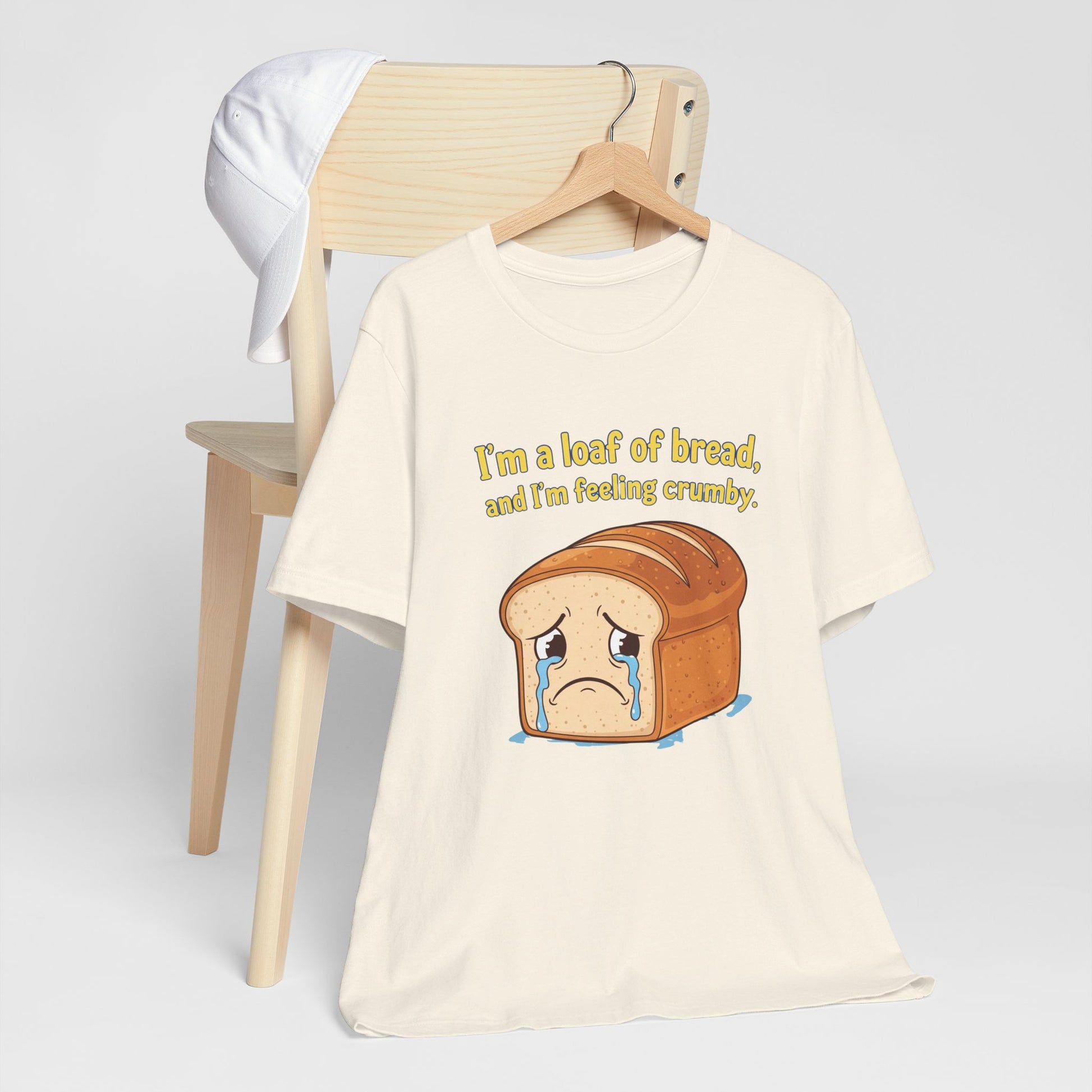 T-shirt with bread graphic and text on a chair against a white background. The text says, "I'm a loafing of bread, and I'm feeling crumby."