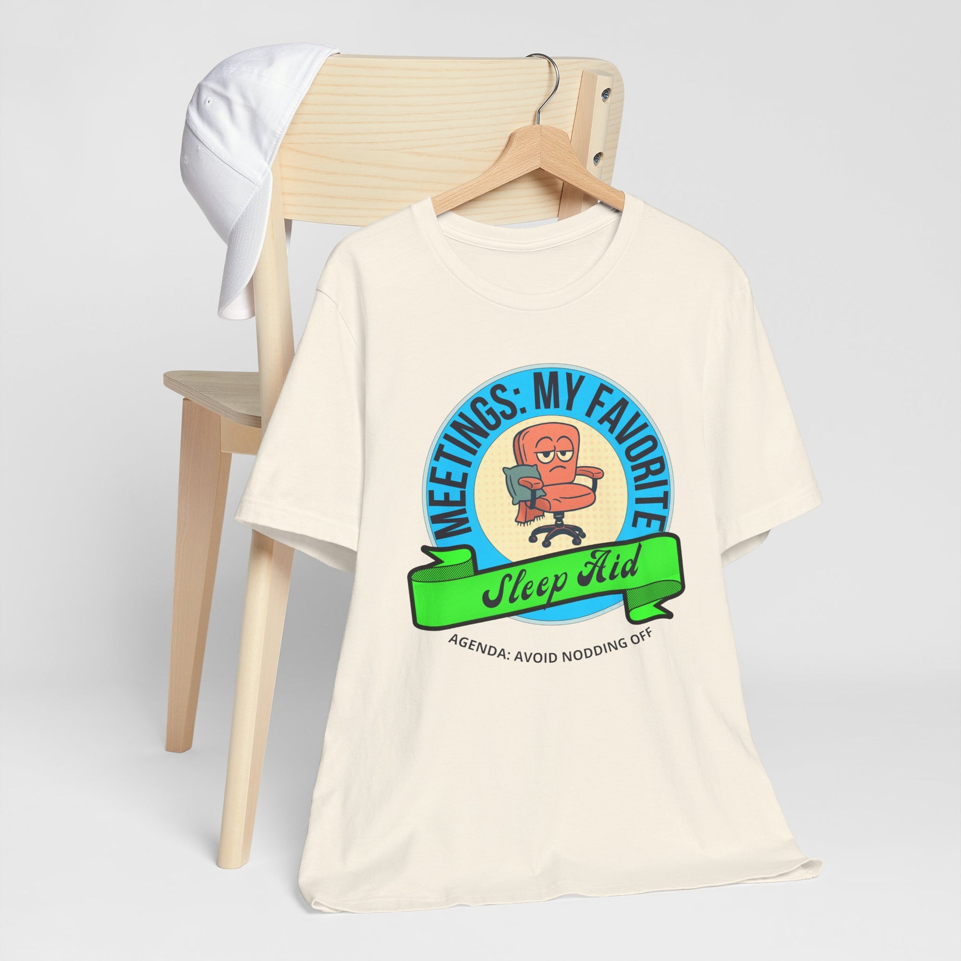 Beige t-shirt with a graphic design and text 'Meetings: My favorite sleep aid. Agenda: Avoid nodding off' on a white background
