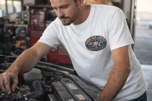 Man working on a car engine wearing a white t-shirt with a 'Slick Rick Lubes' logo.