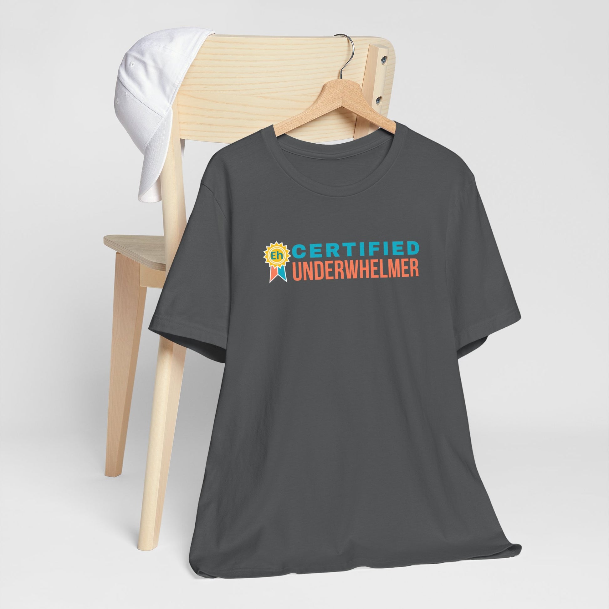 Gray t-shirt with 'Certified Underwhelmer' text on a wooden chair against a white background