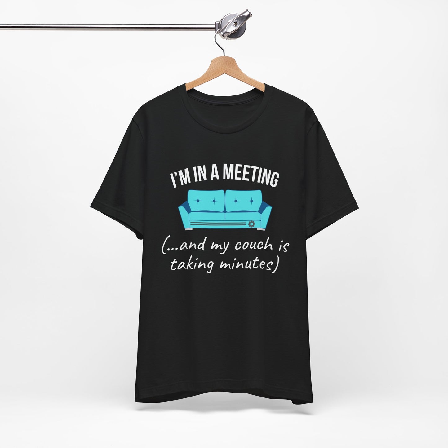 Black t-shirt with humorous graphic and text 'I'm in a meeting (...and my couch is taking minutes)' on a hanger against a white background