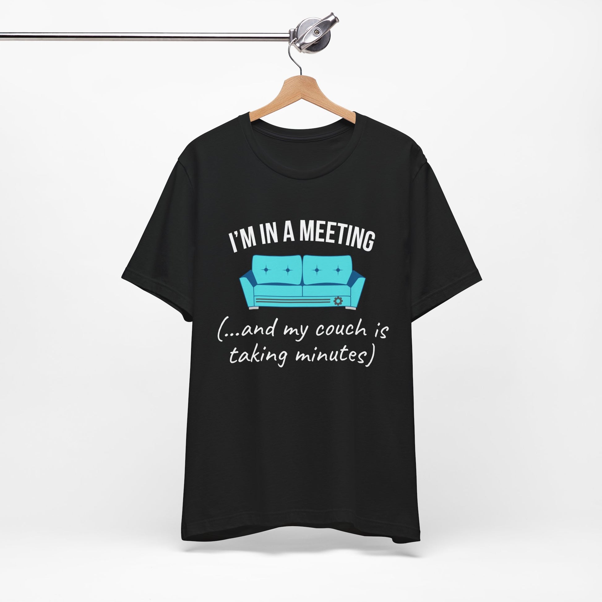 Black t-shirt with humorous graphic and text 'I'm in a meeting (...and my couch is taking minutes)' on a hanger against a white background