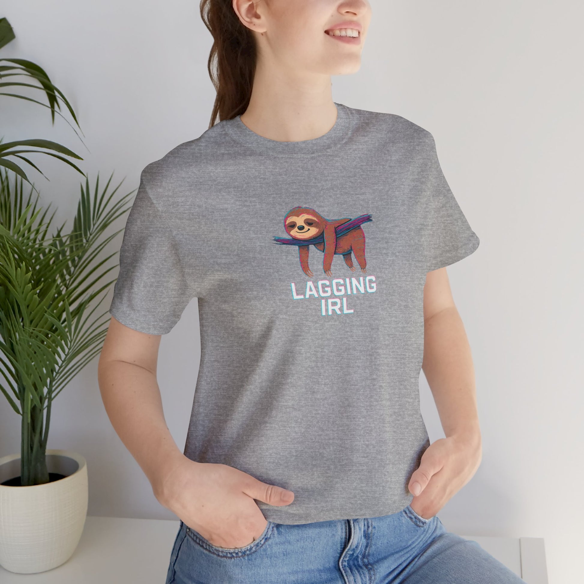 Person wearing a gray t-shirt with a sloth graphic and text 'Lagging IRL', standing indoors next to a plant.