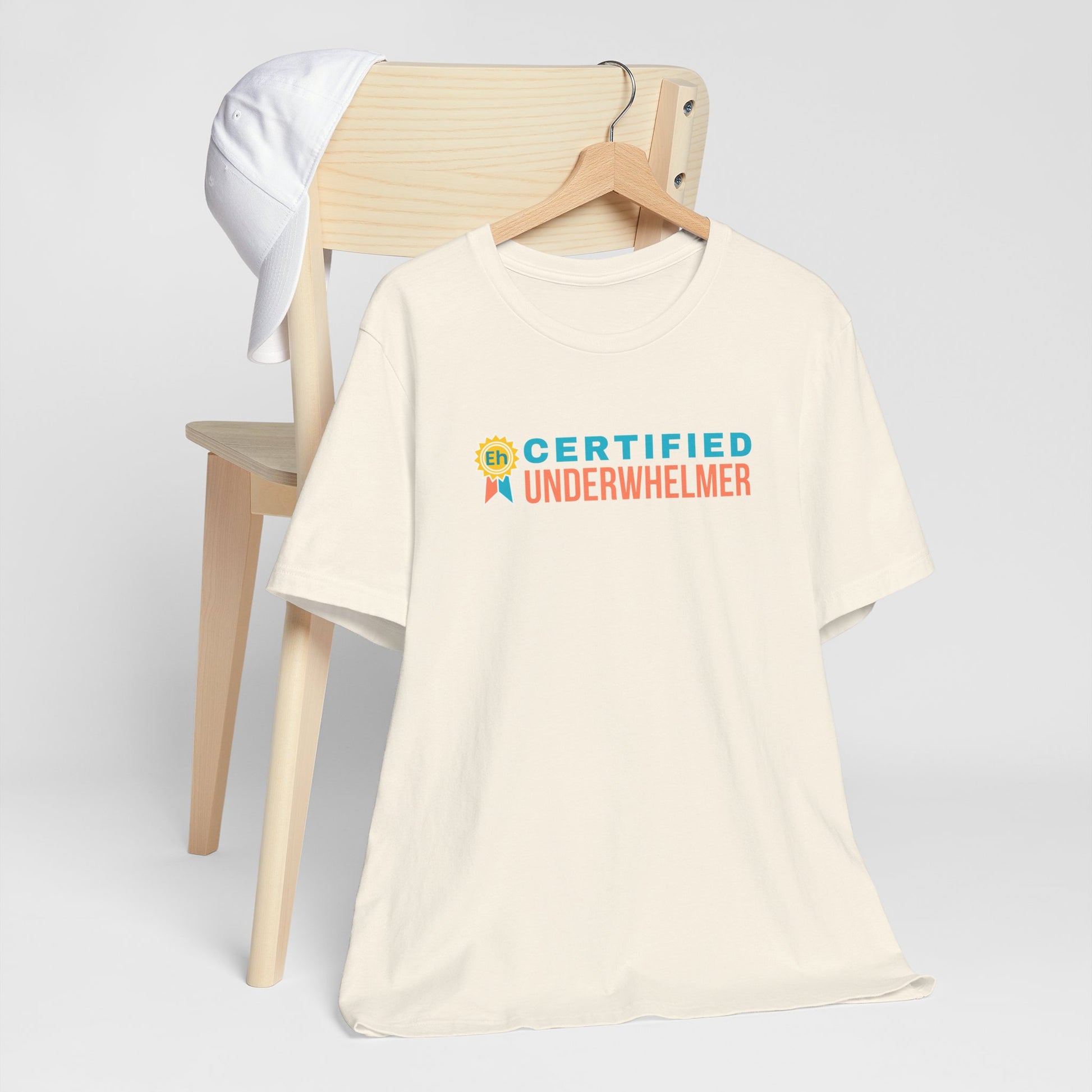 Beige t-shirt with 'Certified Underwhelmer' text on a white background