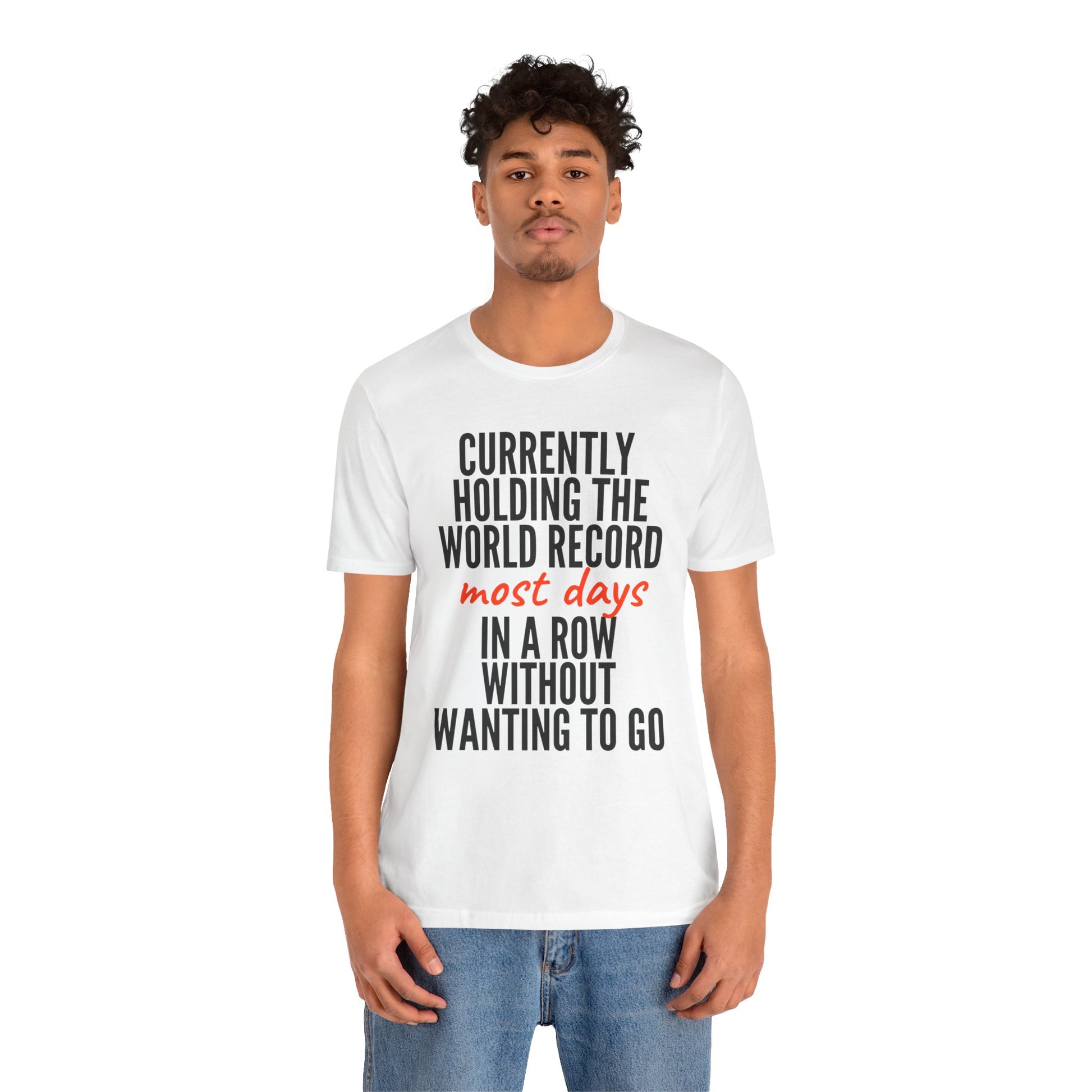 Person wearing a white t-shirt with humorous text 'Currently holding the world record most days in a row without wanting to go' design on a white background