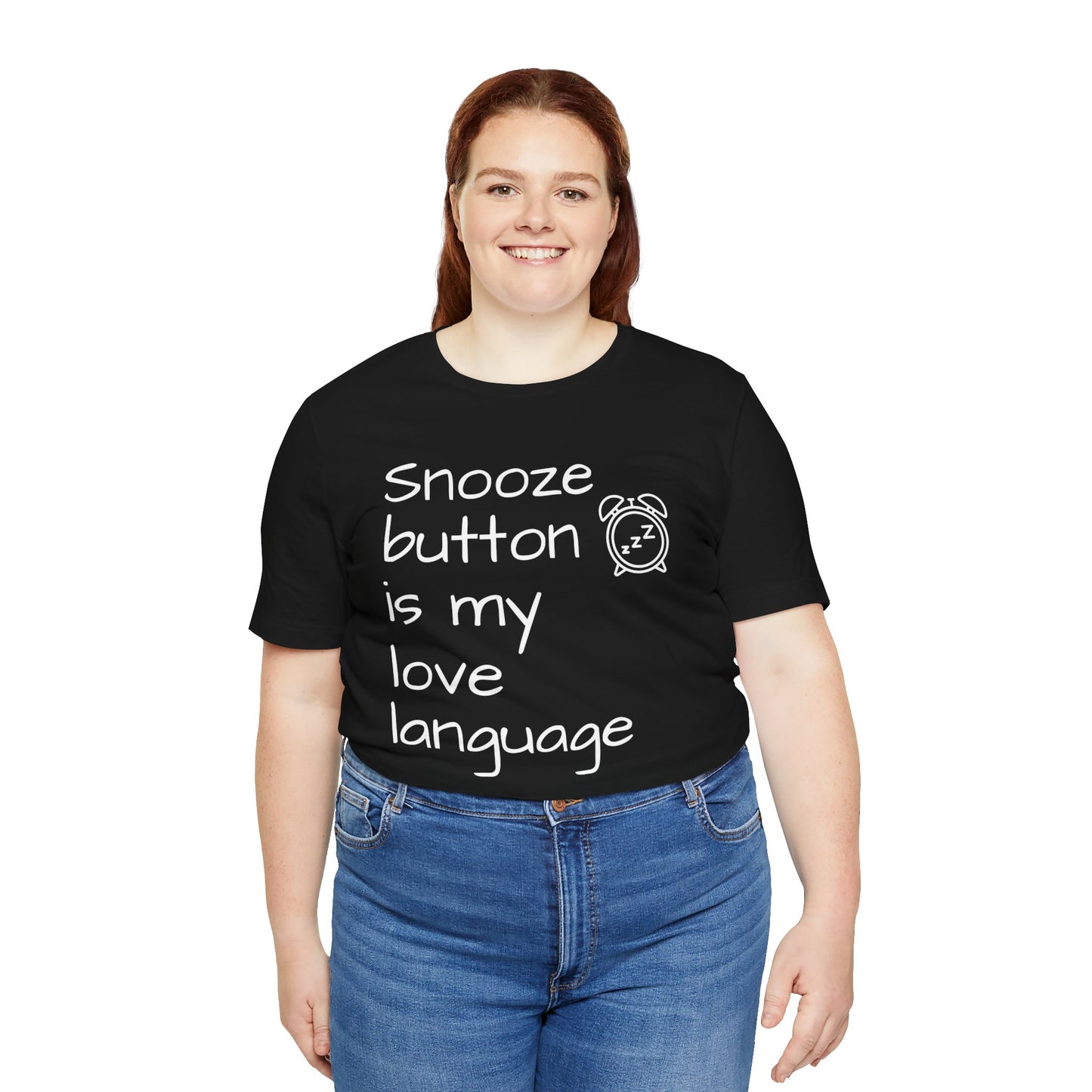 Person wearing a black t-shirt with text 'Snooze button is my love language' and blue jeans on a white background