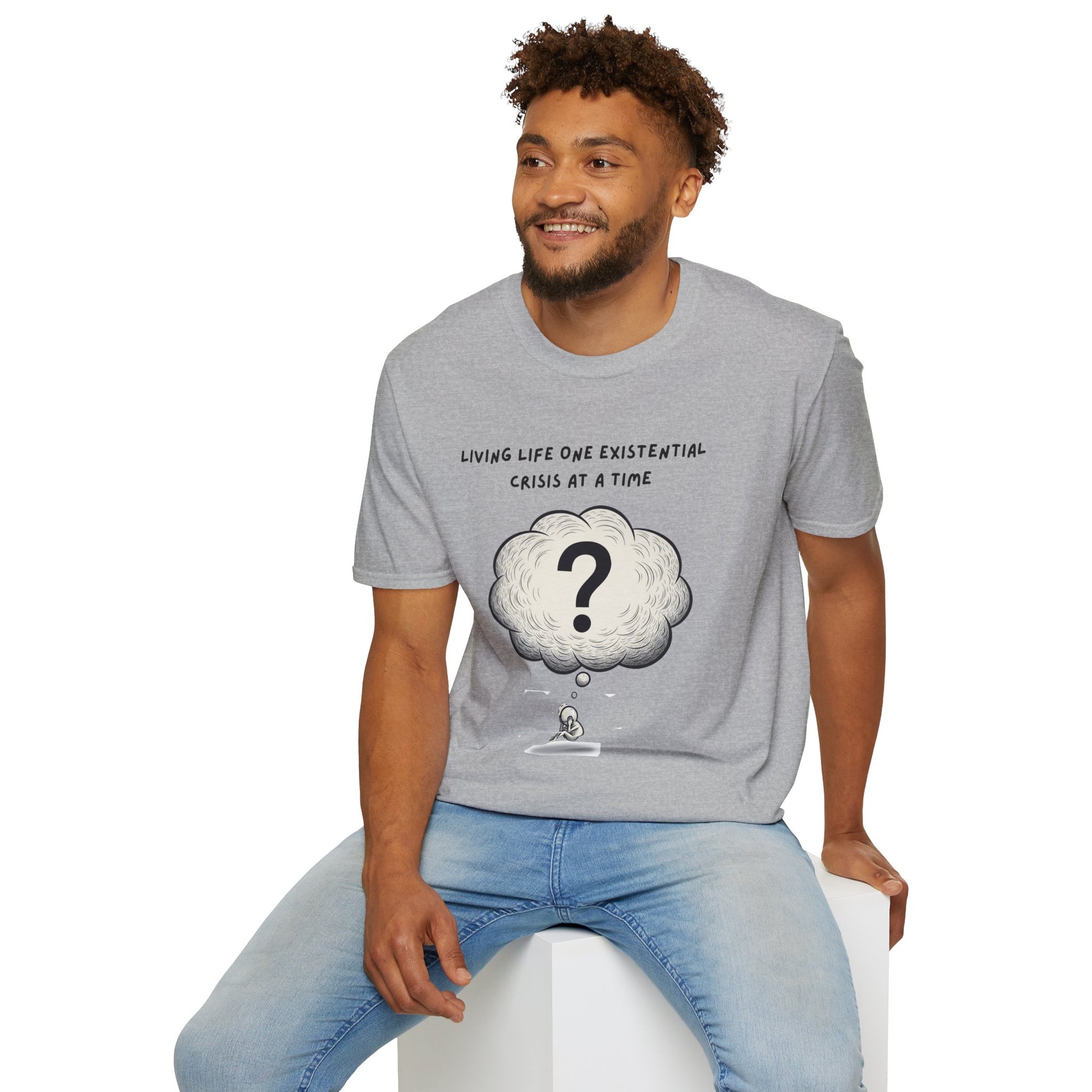 Man wearing a gray t-shirt with a graphic and text 'Living Life One Existential Crisis At A Time', sitting on a white stool against a white background.