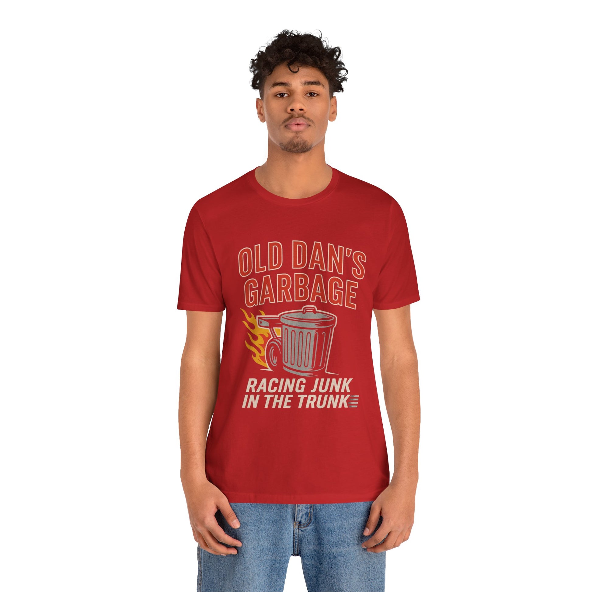 Person wearing a red graphic T‑shirt featuring the bold red and white text “Old Dan’s Garbage” above a flaming garbage can illustration, with the tagline “Racing Junk in the Trunk” below. Funny drag racing parody shirt with retro racing flames, checkered flag background, and humor‑driven hot rod style, perfect for car enthusiasts and gearhead apparel fans.