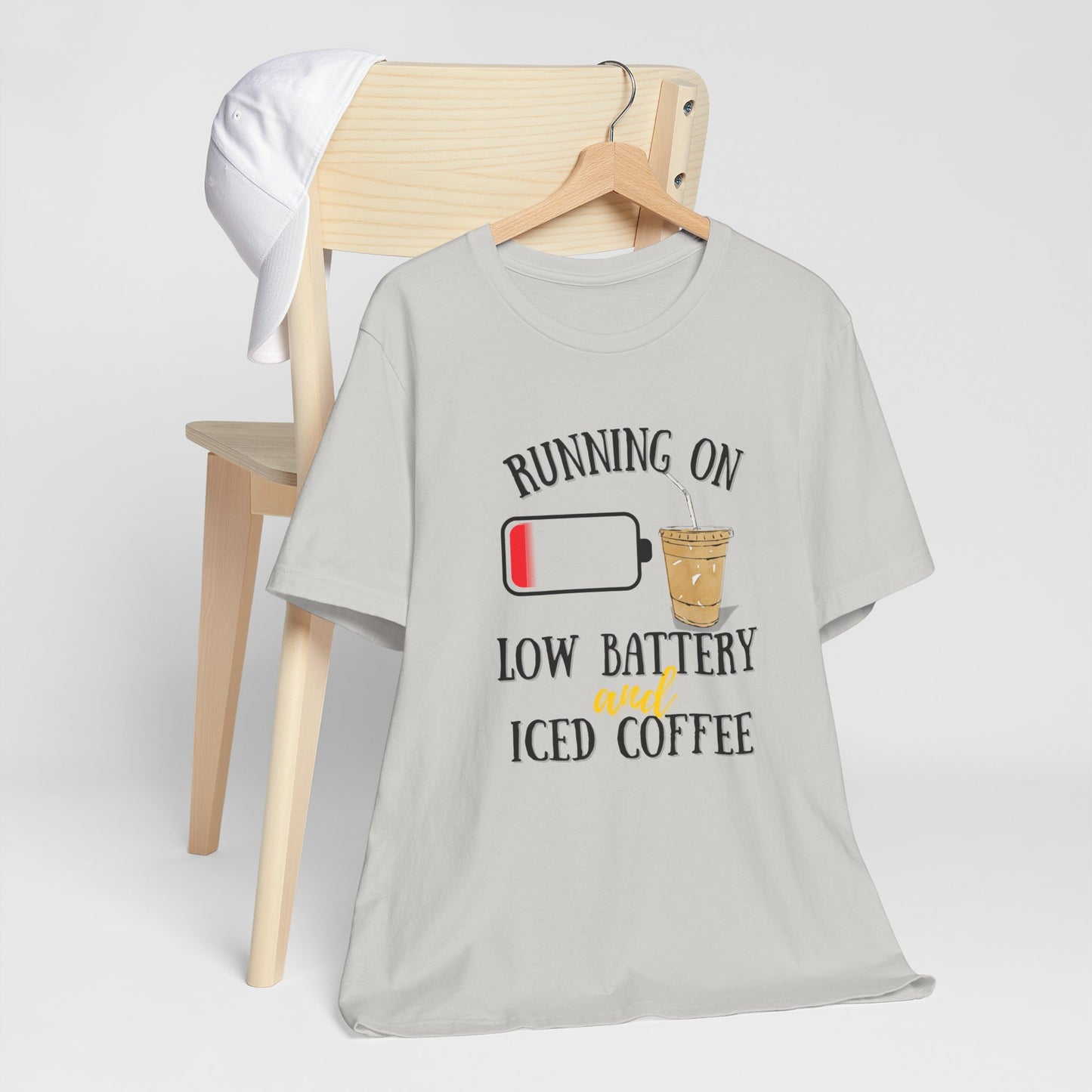 Gray t-shirt with 'Running on low battery and iced coffee' graphic on a wooden chair.