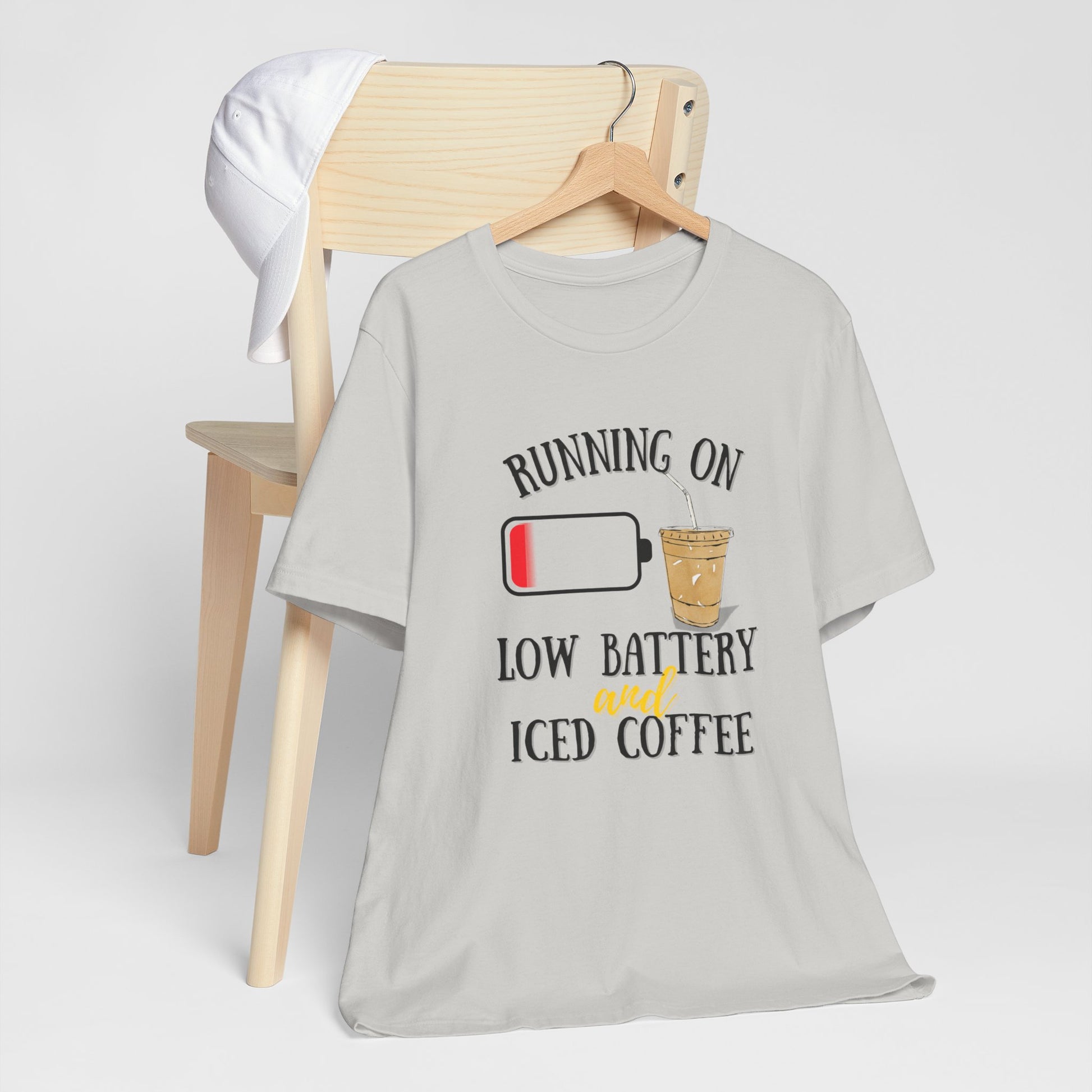 Gray t-shirt with 'Running on low battery and iced coffee' graphic on a wooden chair.