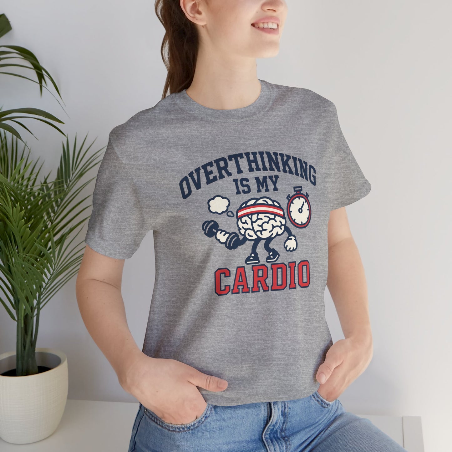 Person wearing a gray t-shirt with a humorous graphic and text 'Overthinking is my cardio', standing indoors next to a plant.