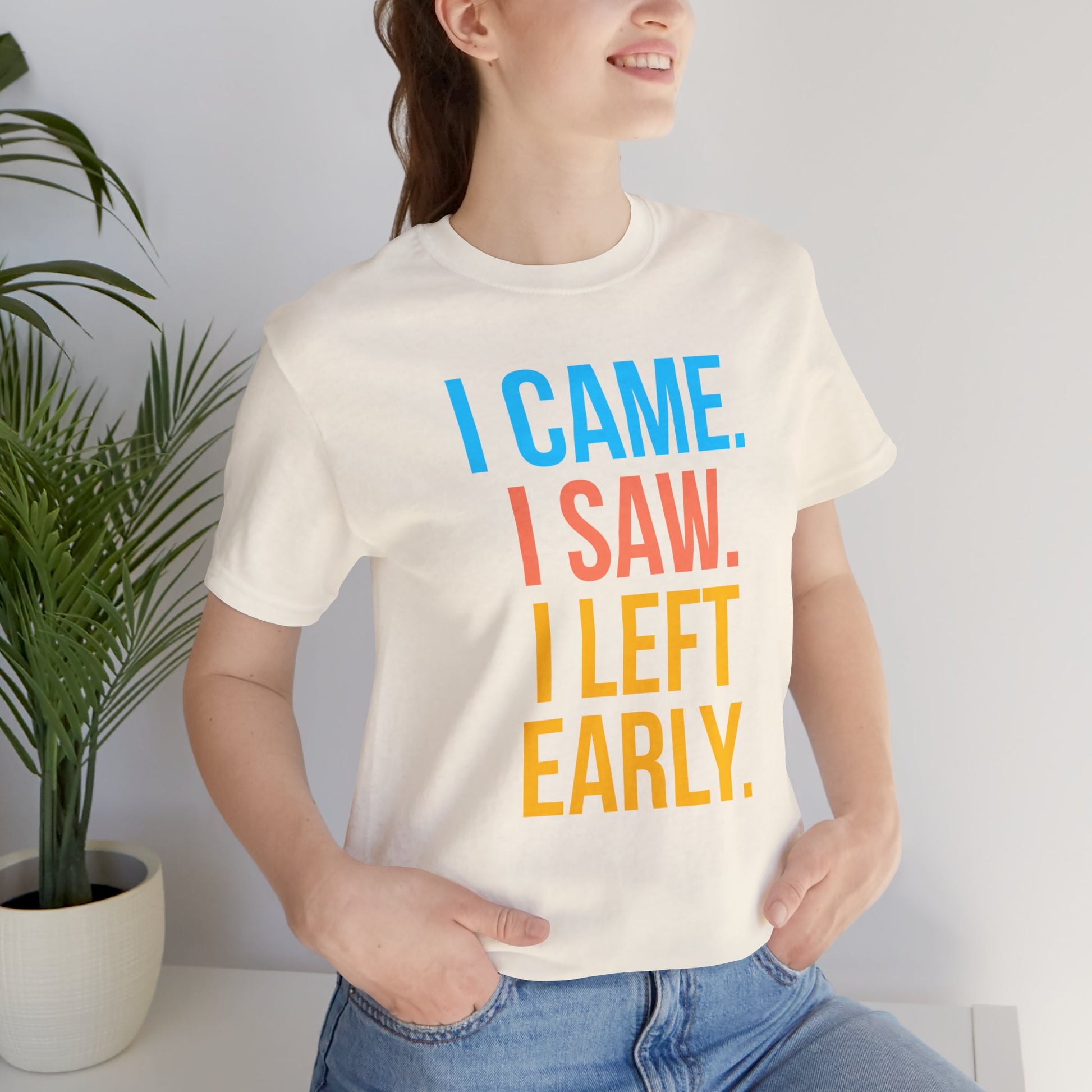 Person wearing a white t-shirt with colorful text 'I CAME. I SAW. I LEFT EARLY.' in a casual setting.