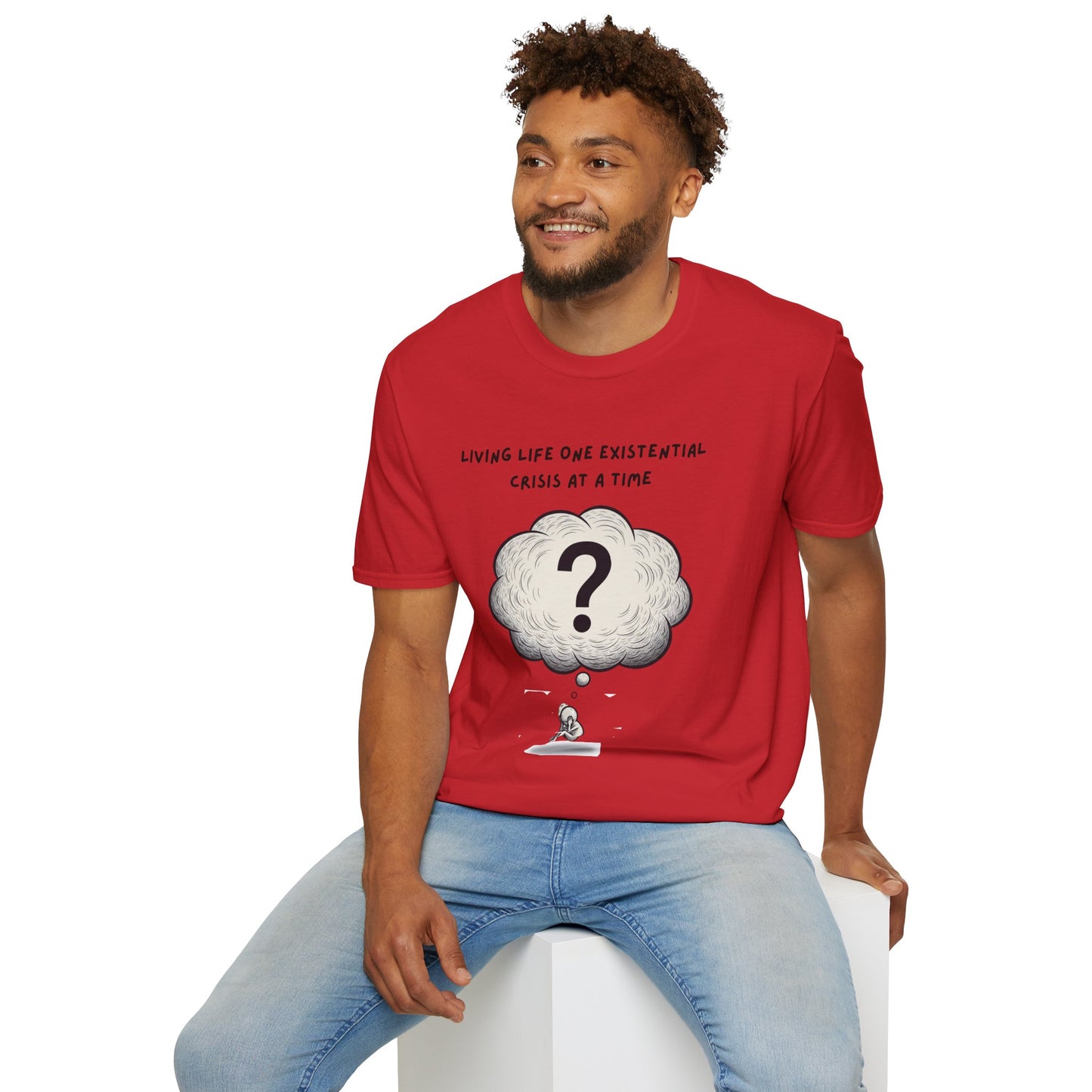 Man wearing a red t-shirt with a graphic and text 'Living Life One Existential Crisis At A Time', sitting on a white stool against a white background.