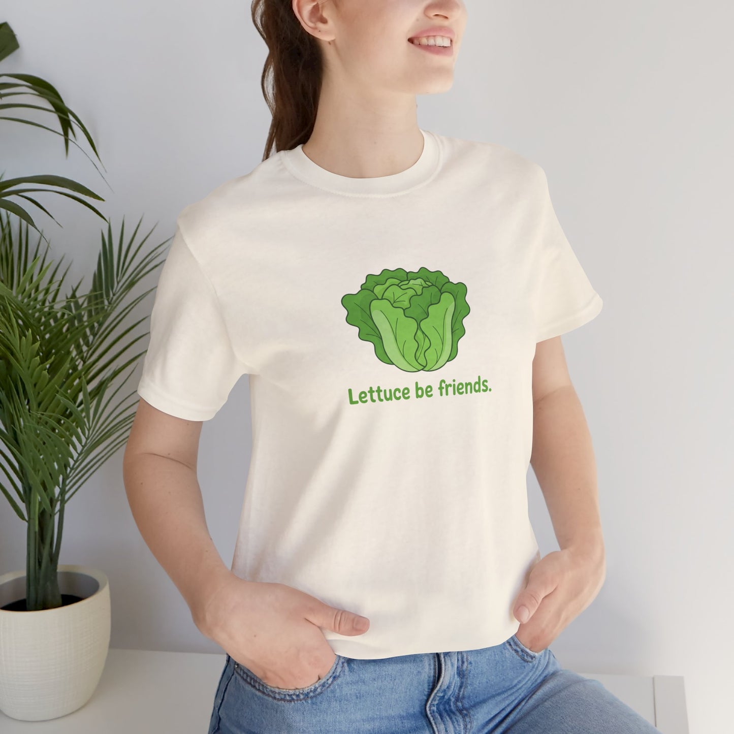 Person wearing a white t-shirt with a green lettuce graphic and text 'Lettuce be friends', standing next to a plant.
