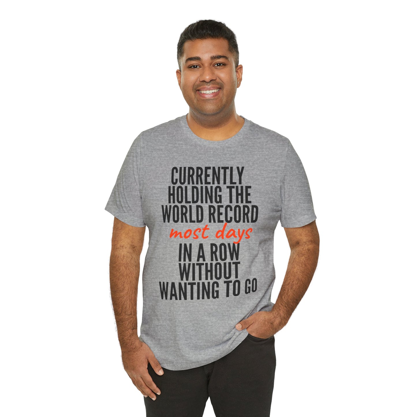 Man wearing a gray t-shirt with humorous text  'Currently holding the world record most days in a row without wanting to go' design on a white background