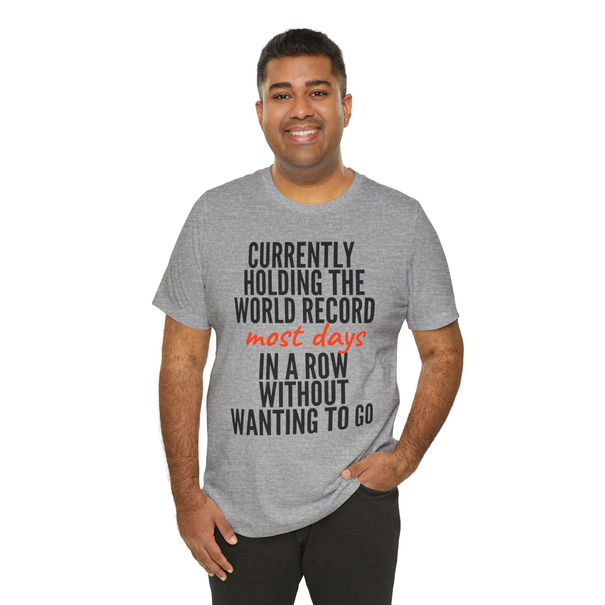 Man wearing a gray t-shirt with humorous text  'Currently holding the world record most days in a row without wanting to go' design on a white background