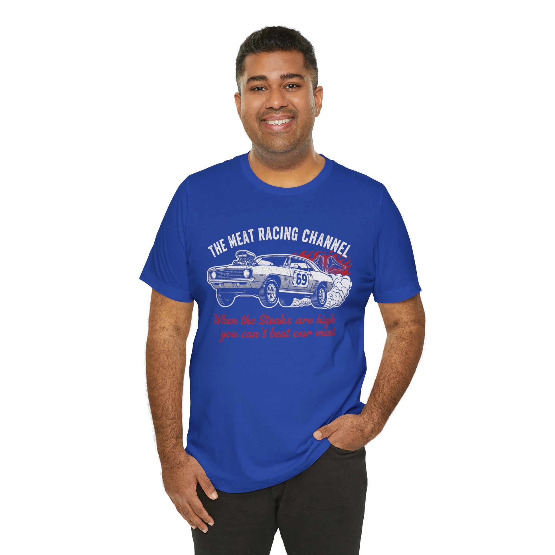 Person wearing a blue Bella+Canvas 3001 T‑shirt featuring a bold drag racing graphic. The design shows a vintage muscle car with the number 69, white smoke and red flames, the distressed white title “The Meat Racing Channel” above, and the red script tagline “When the Steaks are high you can’t beat our meat” below. Funny drag racing parody shirt with retro hot rod style, perfect for car enthusiasts, gearheads, and humor‑driven racing apparel fans.