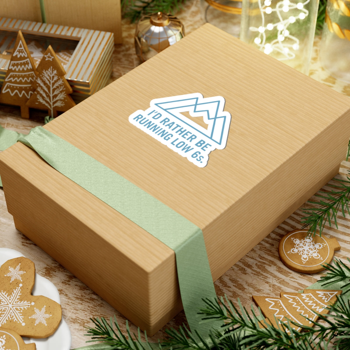 Wooden gift box with a green ribbon and a sticker on a festive background with cookies and lights.