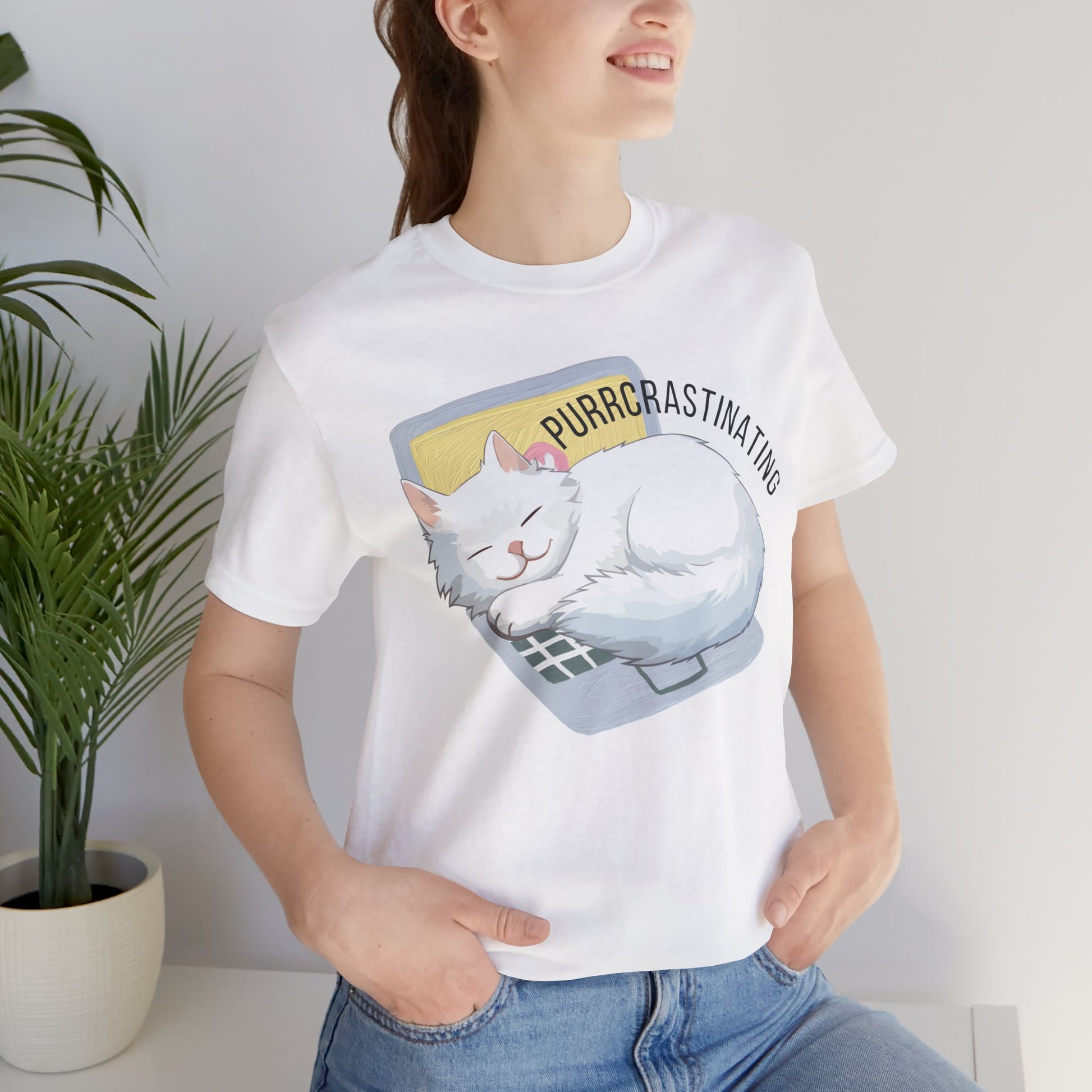 Person wearing a white t-shirt with a cat graphic and text 'Purrcrastinating', standing indoors next to a plant.