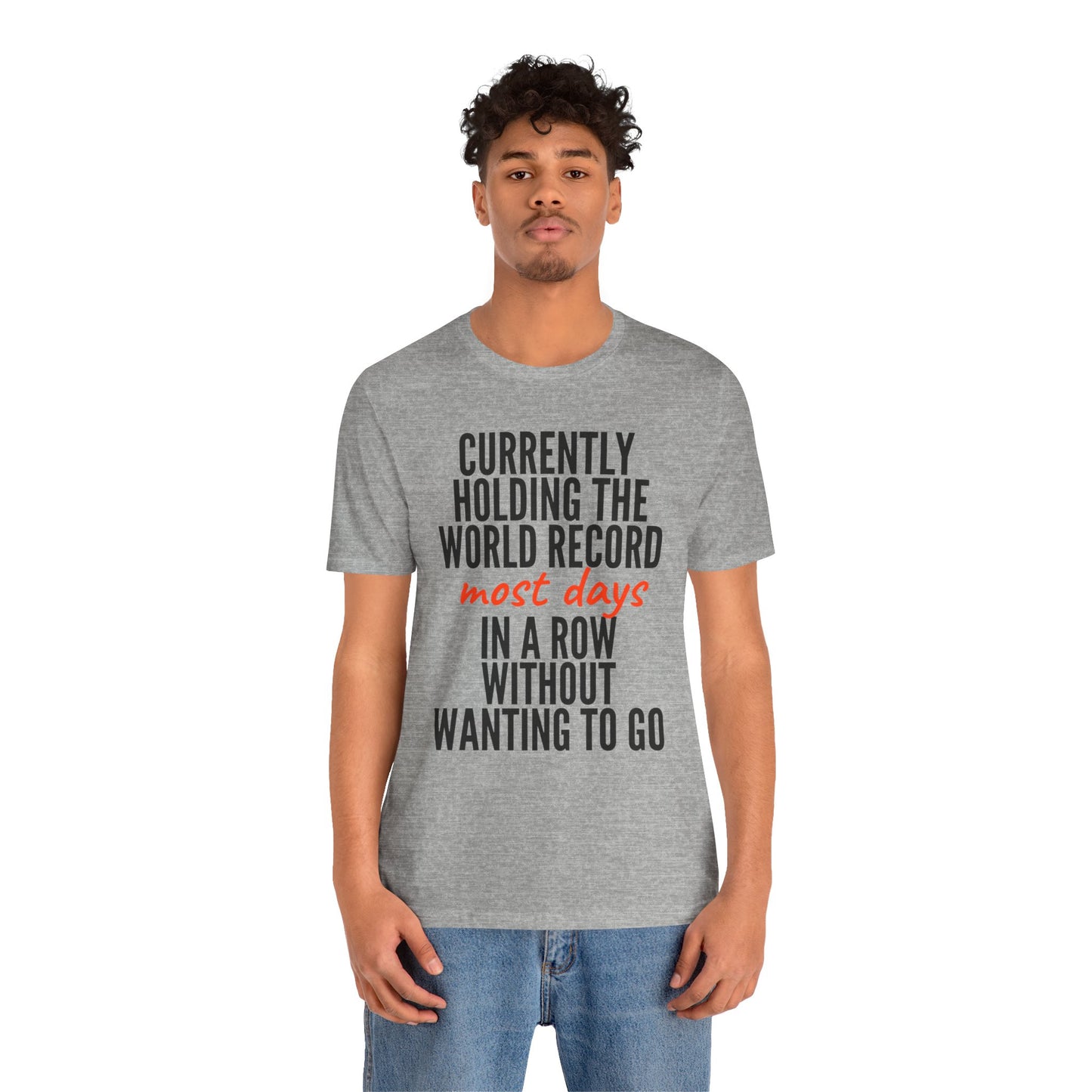 Person wearing a gray t-shirt with humorous text 'Currently holding the world record most days in a row without wanting to go' design on a white background