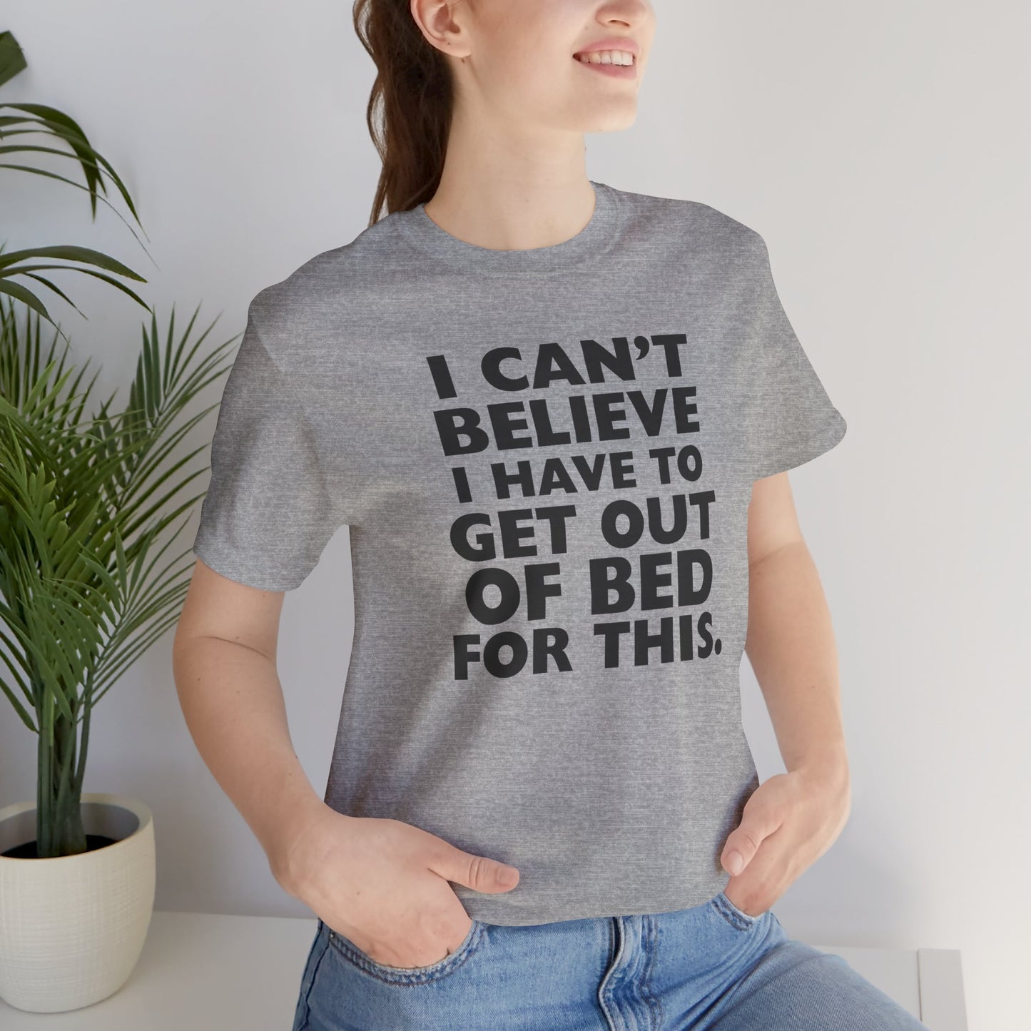 Person wearing a gray t-shirt with black text 'I can't believe I have to get out of bed for this' on a white background