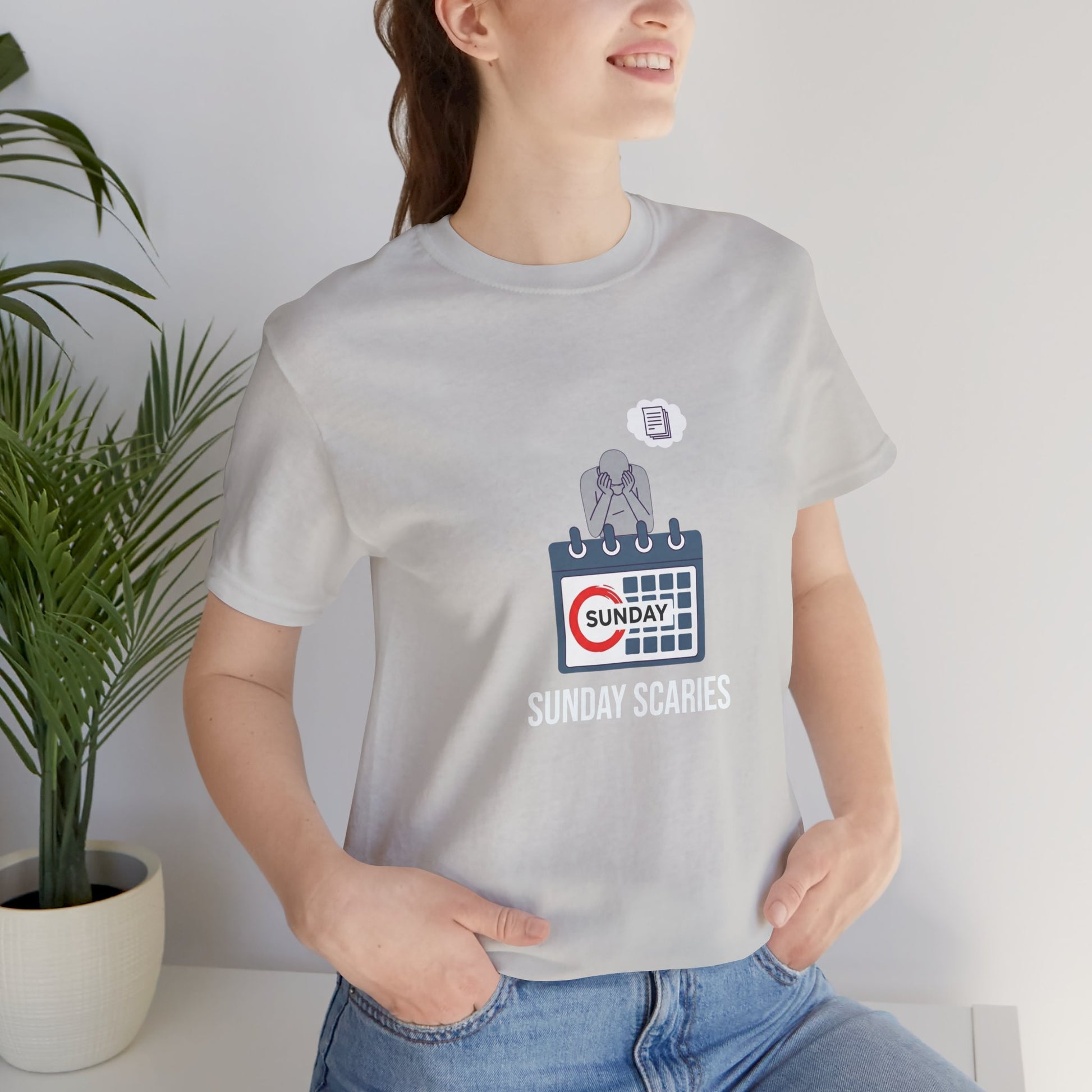 Person wearing a gray t-shirt with a graphic design and text 'Sunday Scaries', standing indoors next to a plant.