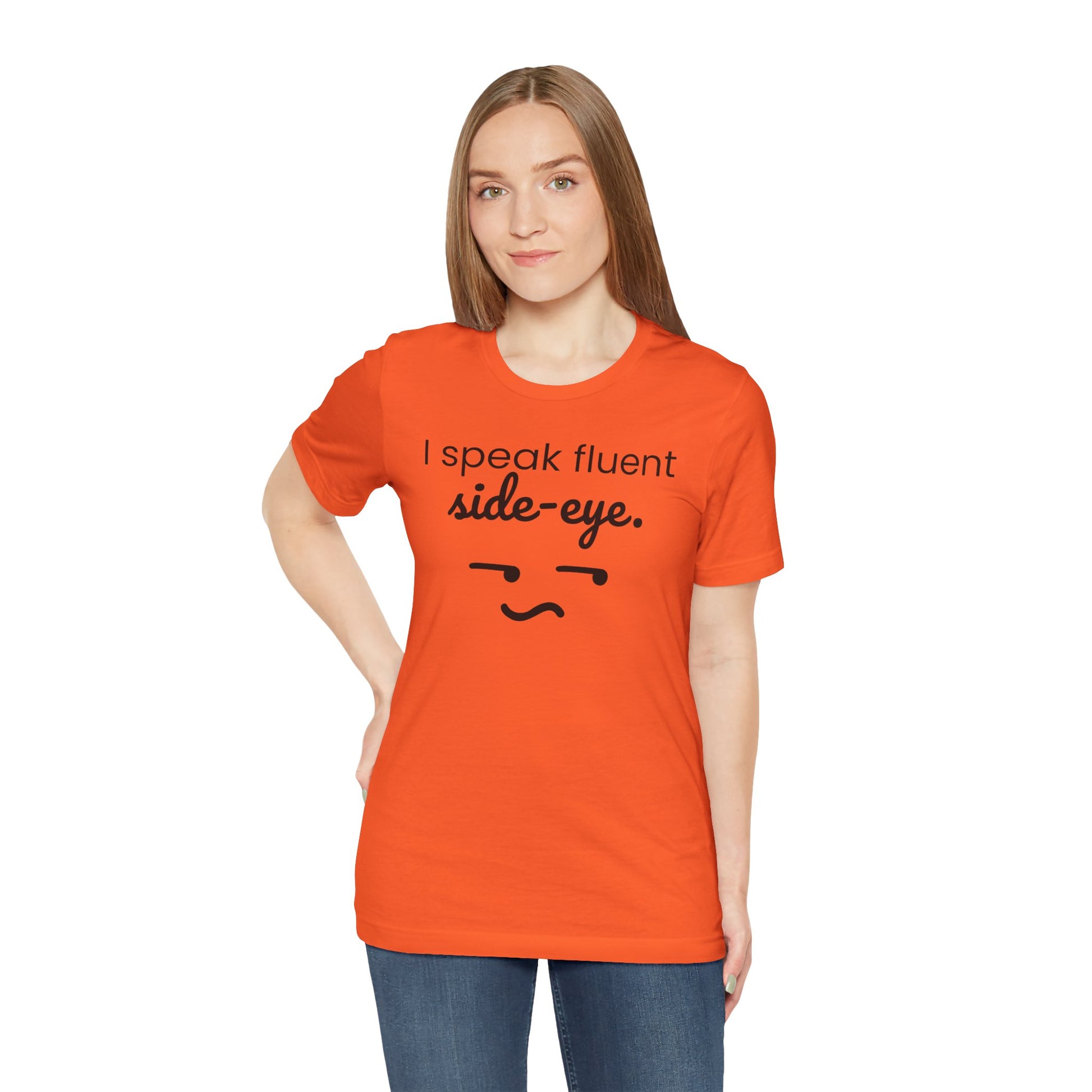 Person wearing an orange t-shirt with text 'I speak fluent side eye' and a smiley face on a white background