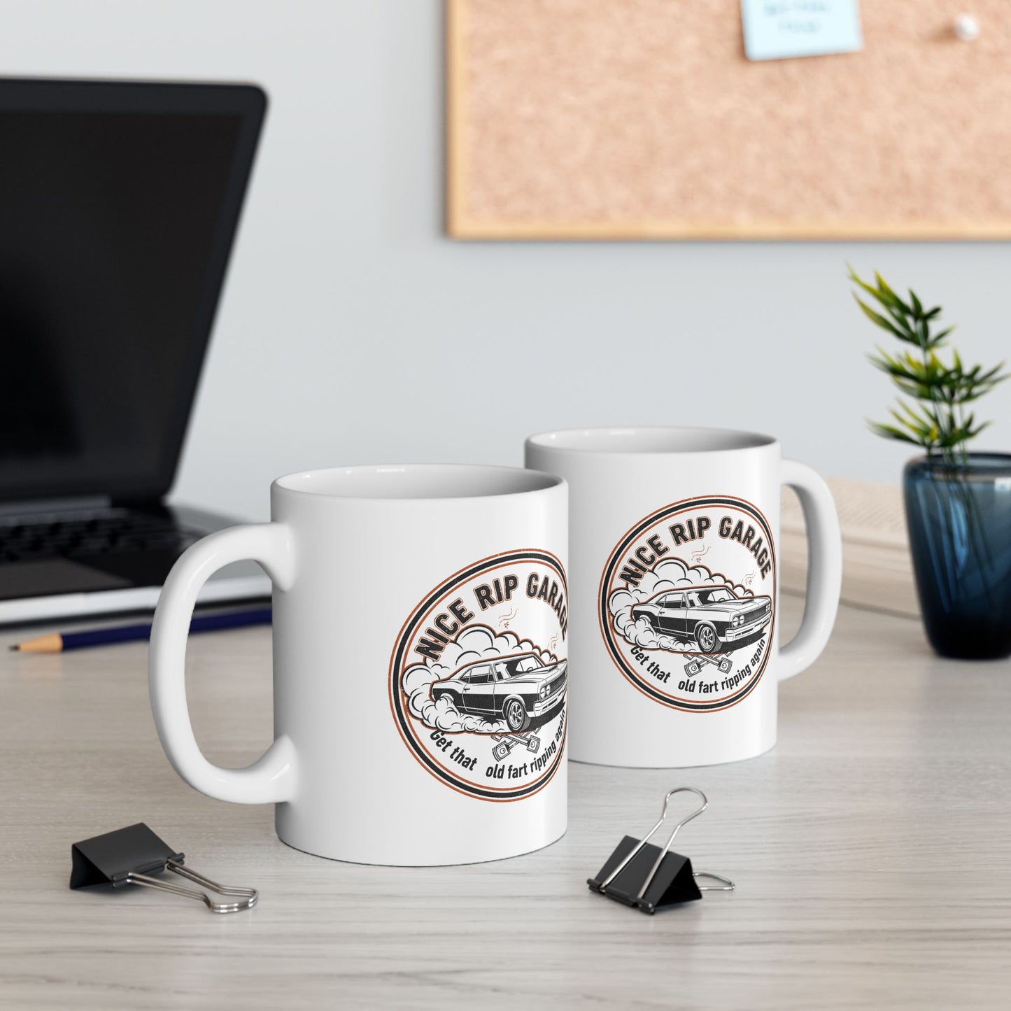Two white mugs with a vintage car design and text 'Nice Rip Garage Get that old fart ripping again' on a desk with office supplies.