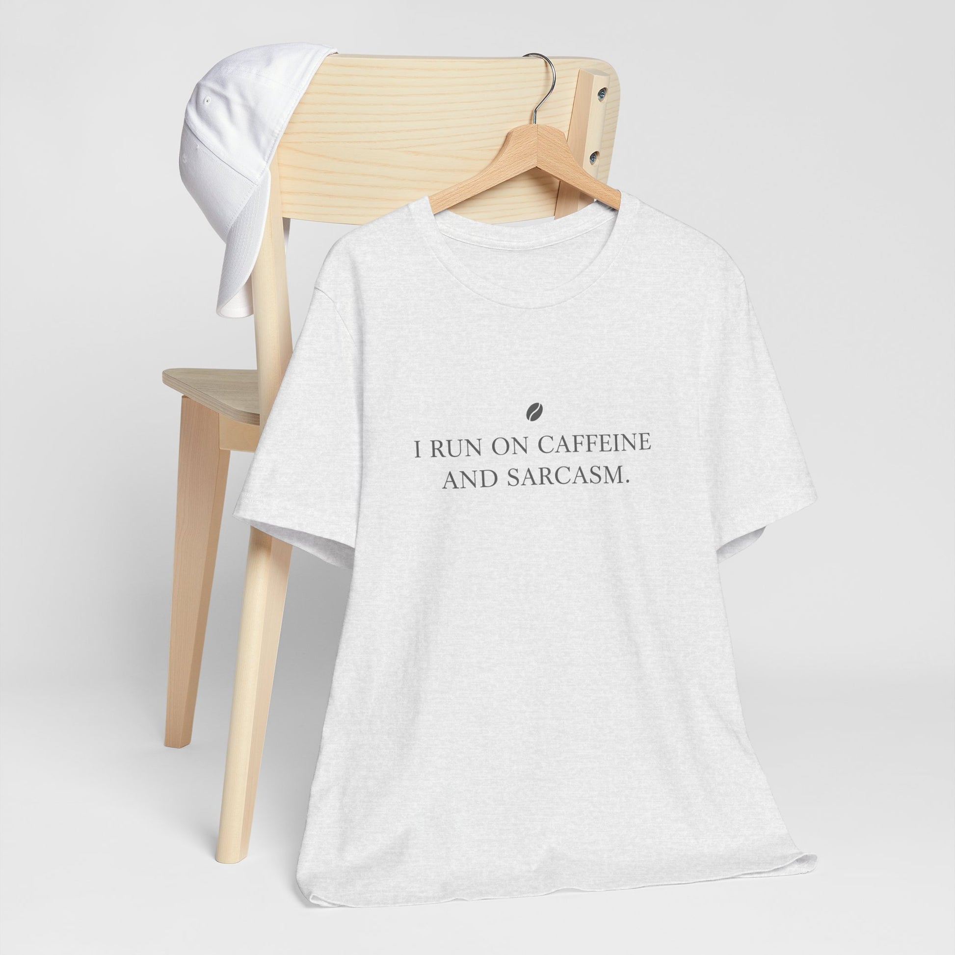White t-shirt with text 'I run on caffeine and sarcasm' on a wooden chair.