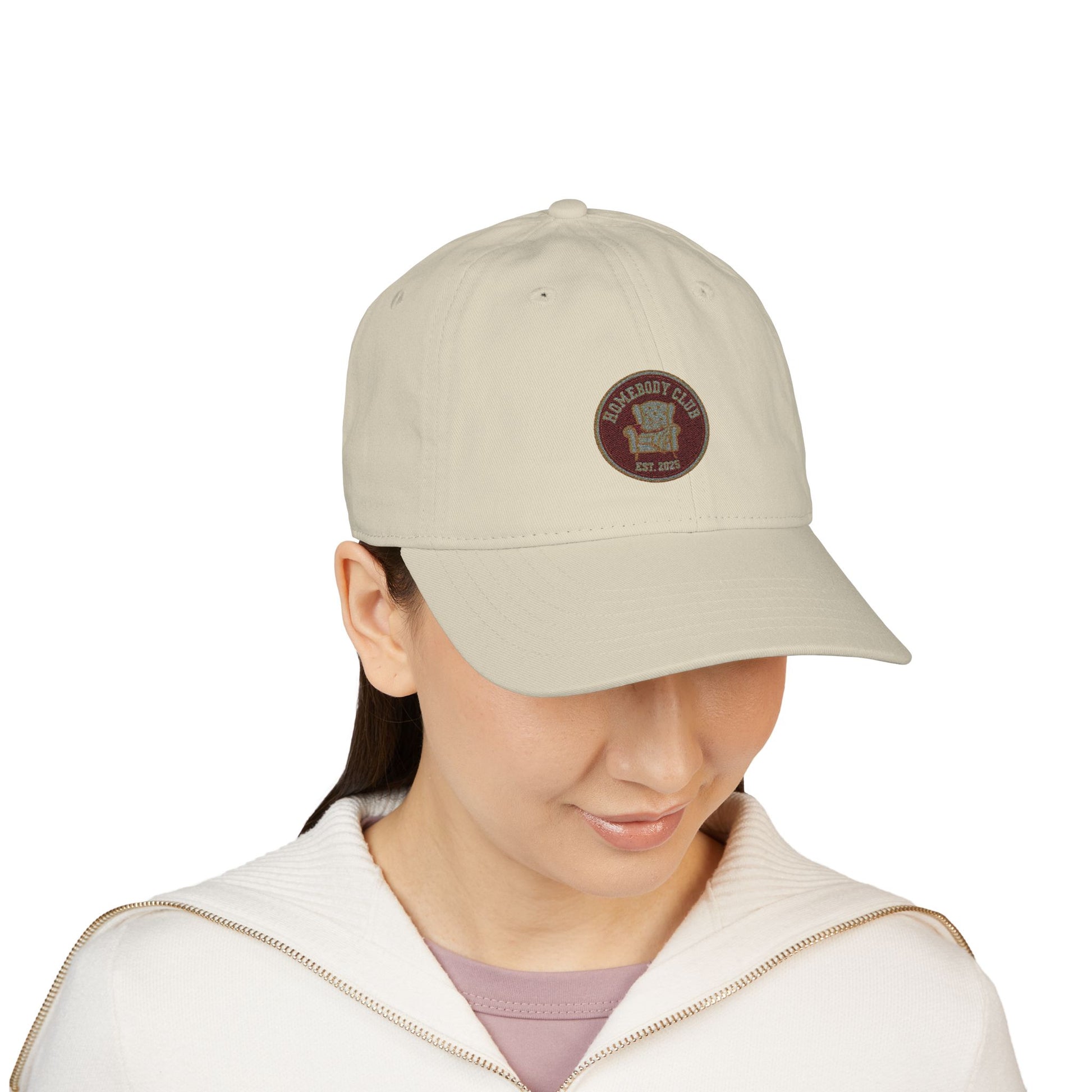 Person wearing a beige cap with a logo and text 'Homebody club Est. 2025' on a white background