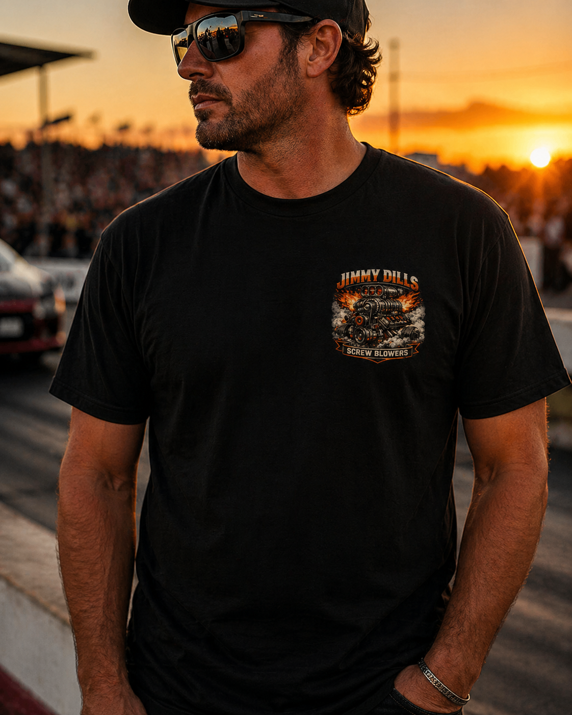 Man wearing a black t-shirt with a Jimmy Dills Screw Blowers logo at a race track during sunset.