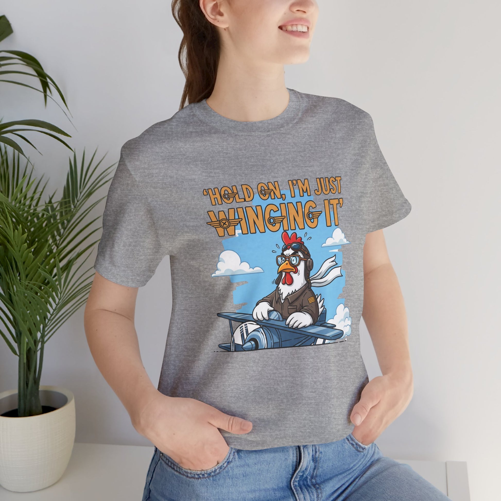 Person wearing a gray t-shirt with a cartoon chicken graphic and text 'Hold on, I'm just winging it'.