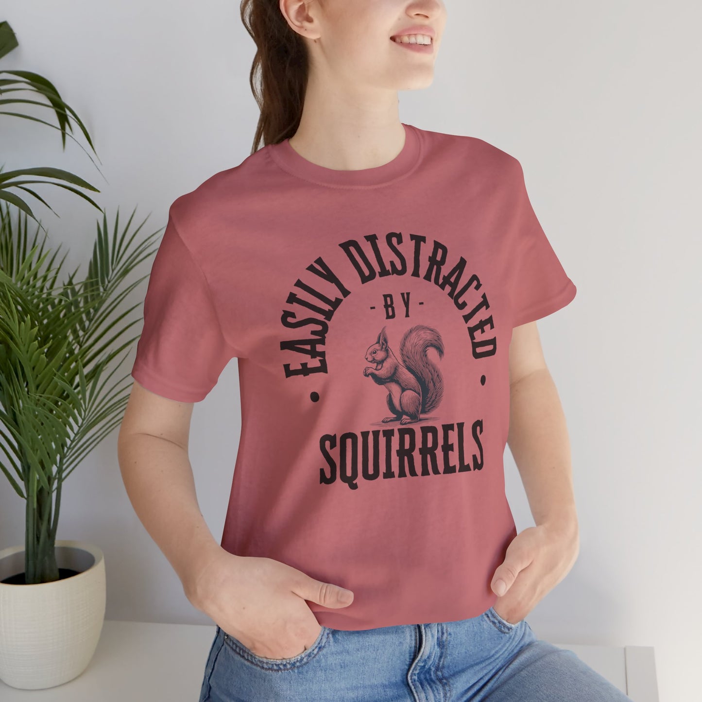 Person wearing a pink t-shirt with a squirrel graphic and text 'EASILY DISTRACTED BY SQUIRRELS', standing indoors.