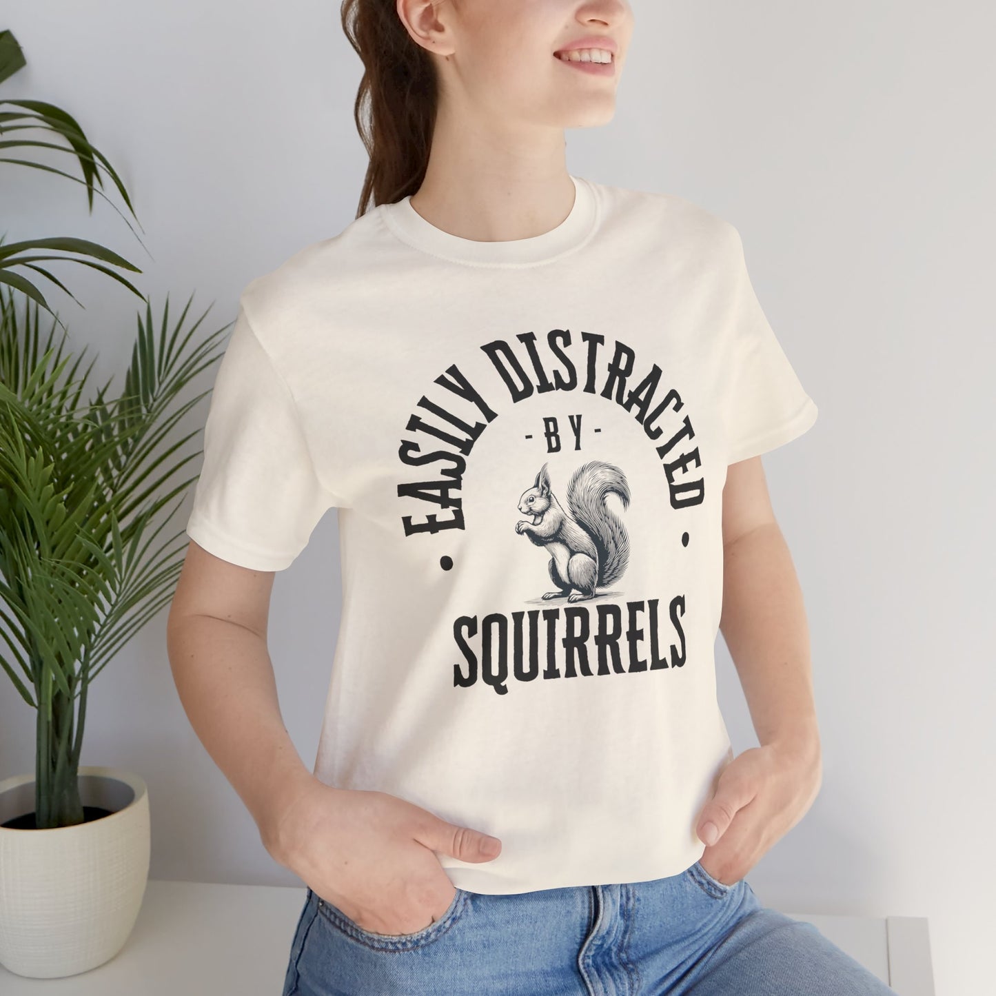 Person wearing a white t-shirt with a squirrel graphic and text 'EASILY DISTRACTED BY SQUIRRELS', standing against a plain background.