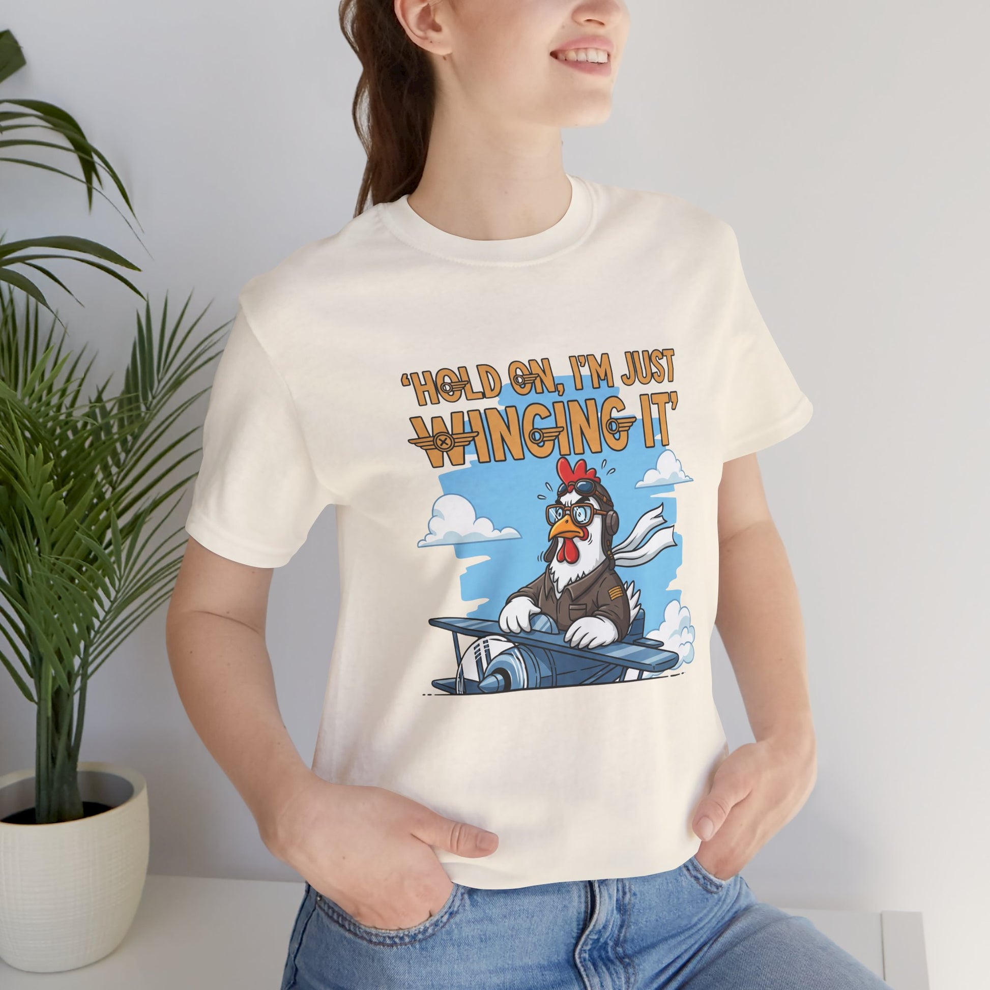 Person wearing a t-shirt with a cartoon chicken on a plane graphic and text 'Hold on, I'm just winging it'.